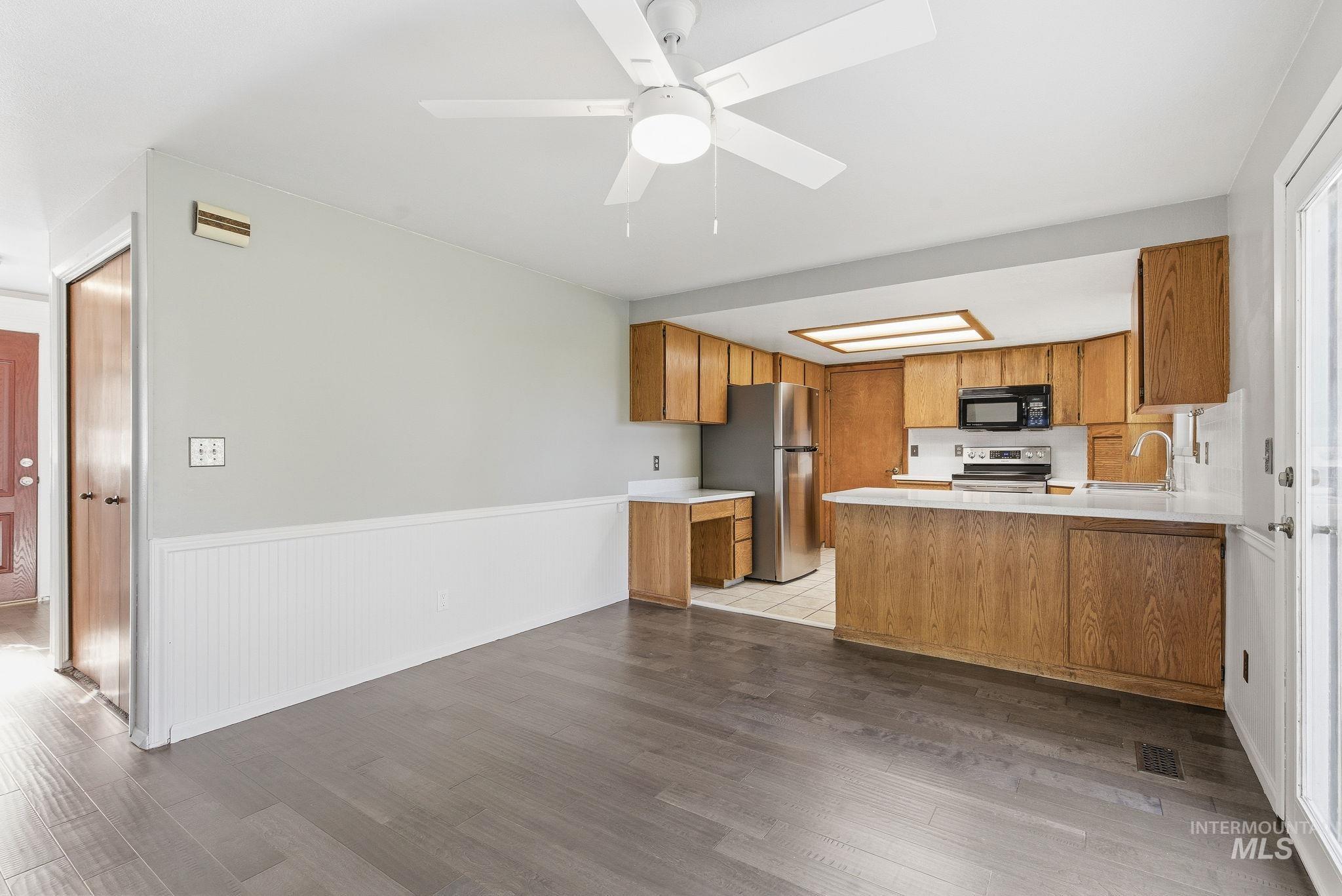 Kitchen featuring a peninsula, light countertops, brown cabinets, stainless steel appliances, and wainscoting