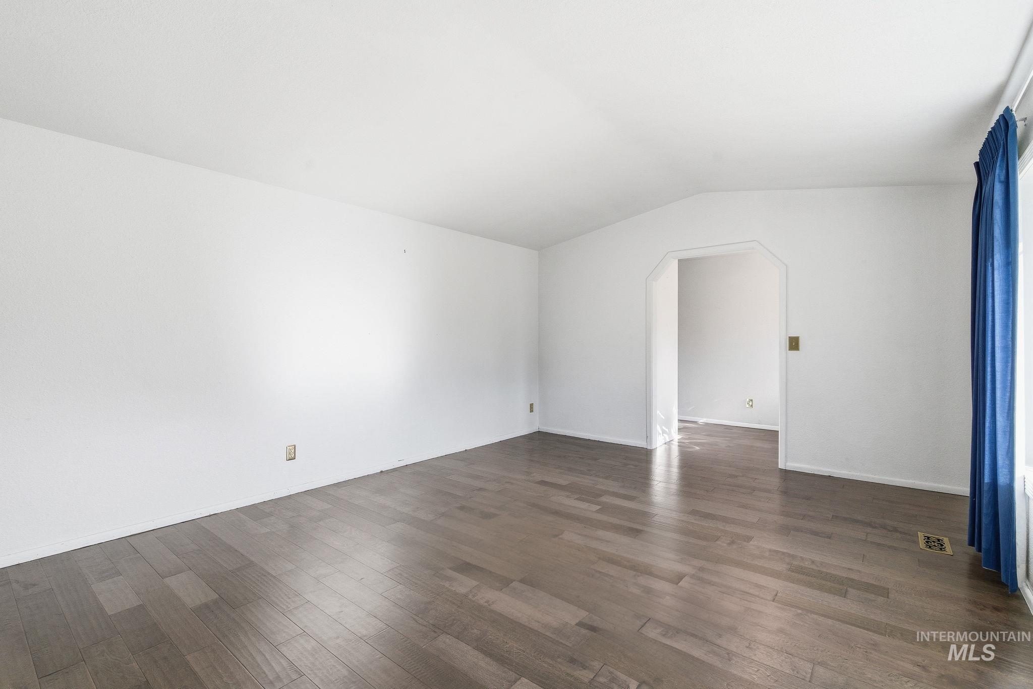 Unfurnished room featuring arched walkways, vaulted ceiling, and dark wood finished floors