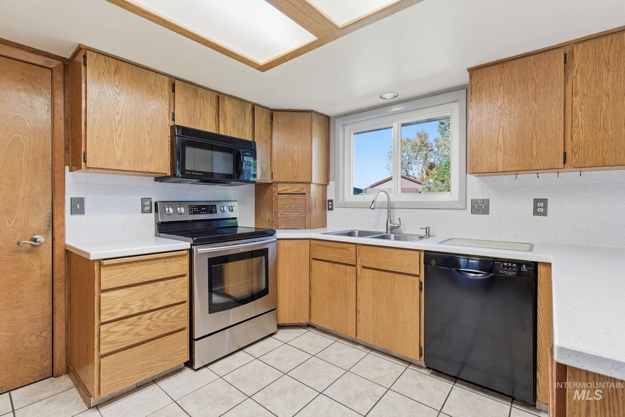 Kitchen featuring black appliances, light countertops, backsplash, and light tile patterned floors