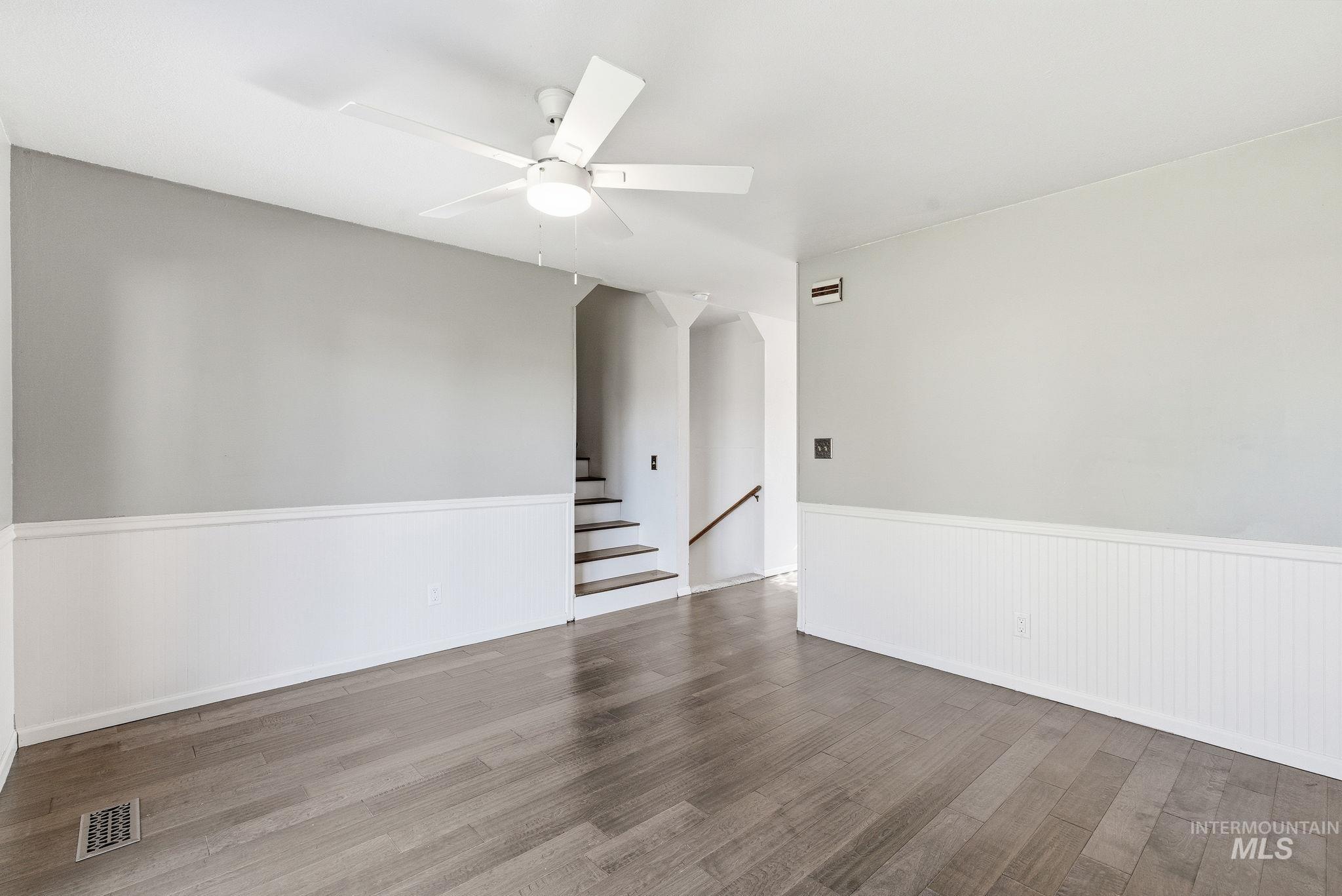 Unfurnished room featuring wood finished floors, ceiling fan, stairway, and a wainscoted wall