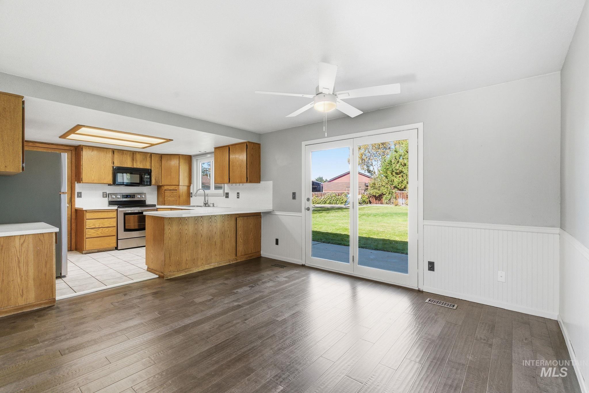 Kitchen featuring light countertops, brown cabinets, stainless steel appliances, a peninsula, and dark wood-style floors