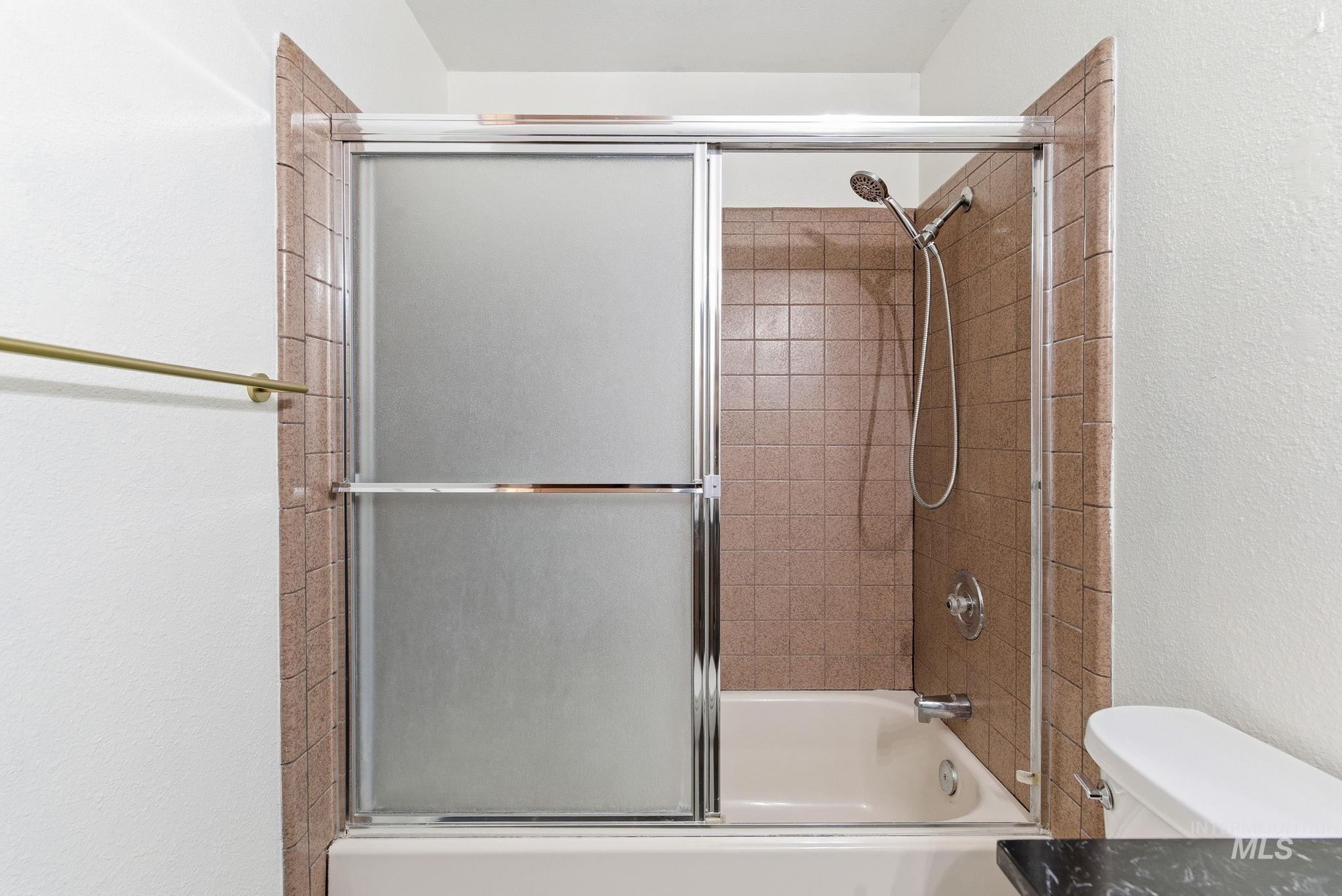 Full bath featuring bath / shower combo with glass door and a textured wall