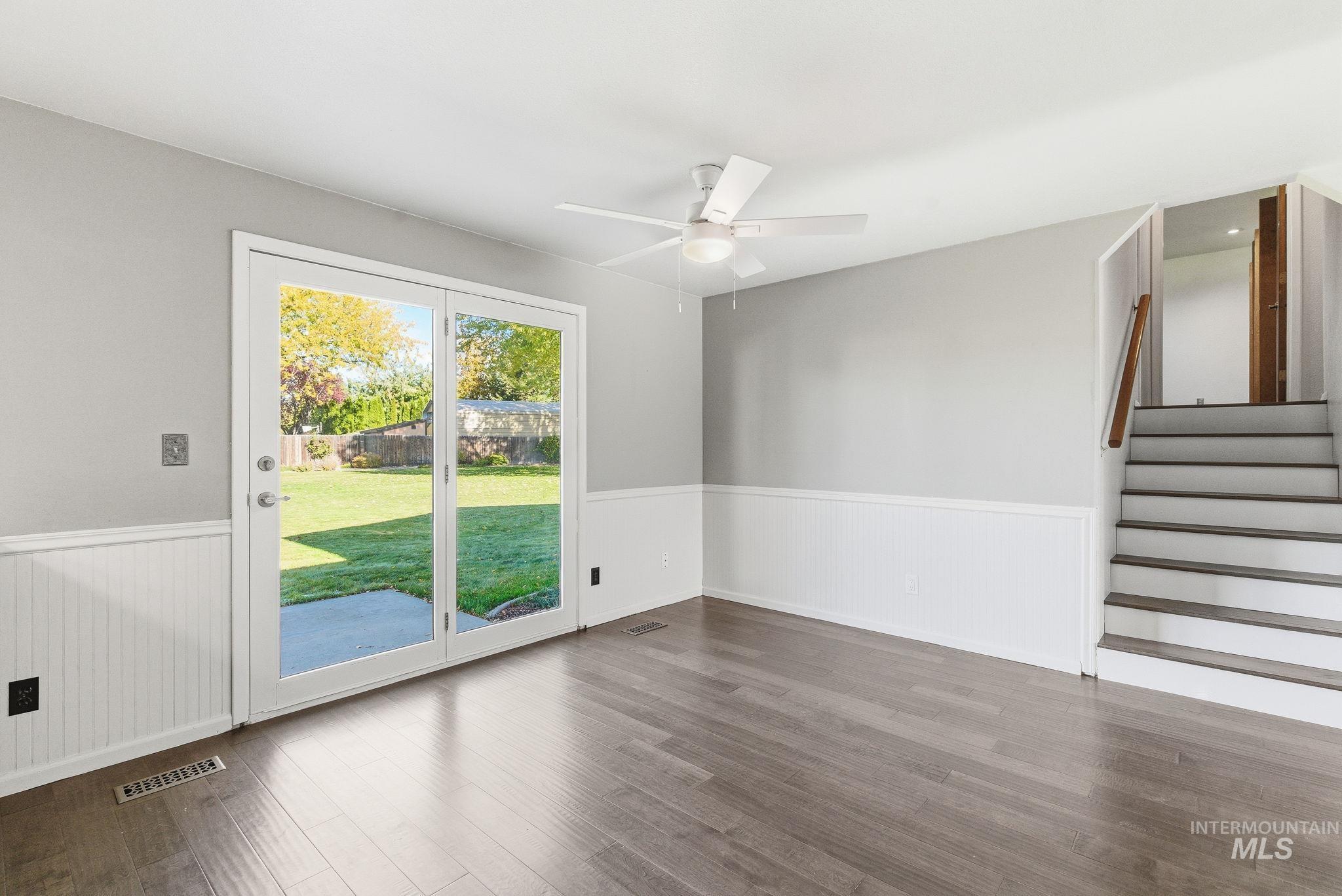 Unfurnished room with stairway, wood finished floors, ceiling fan, and wainscoting
