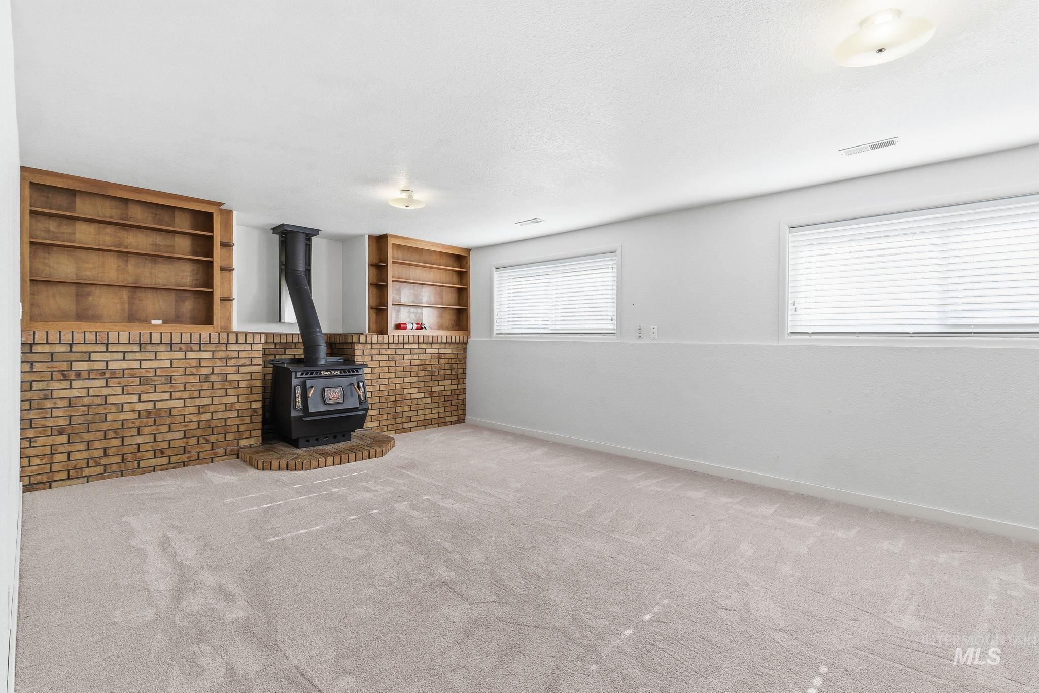 Unfurnished living room with built in shelves, carpet flooring, a wood stove, and a textured ceiling