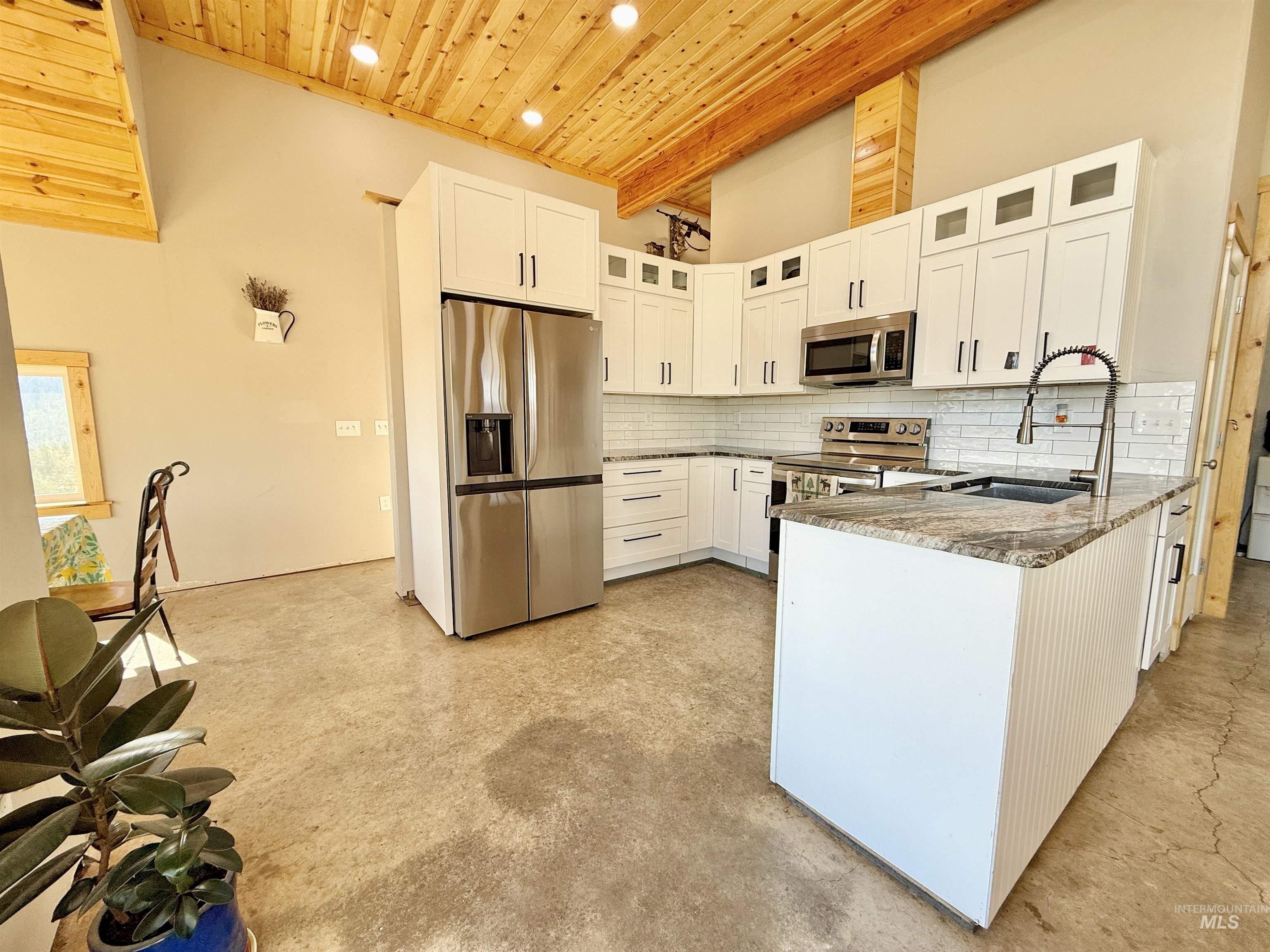 Kitchen with a wood ceiling with exposed beams, dark stone counters, white cabinetry, glass insert cabinets, and stainless steel appliances