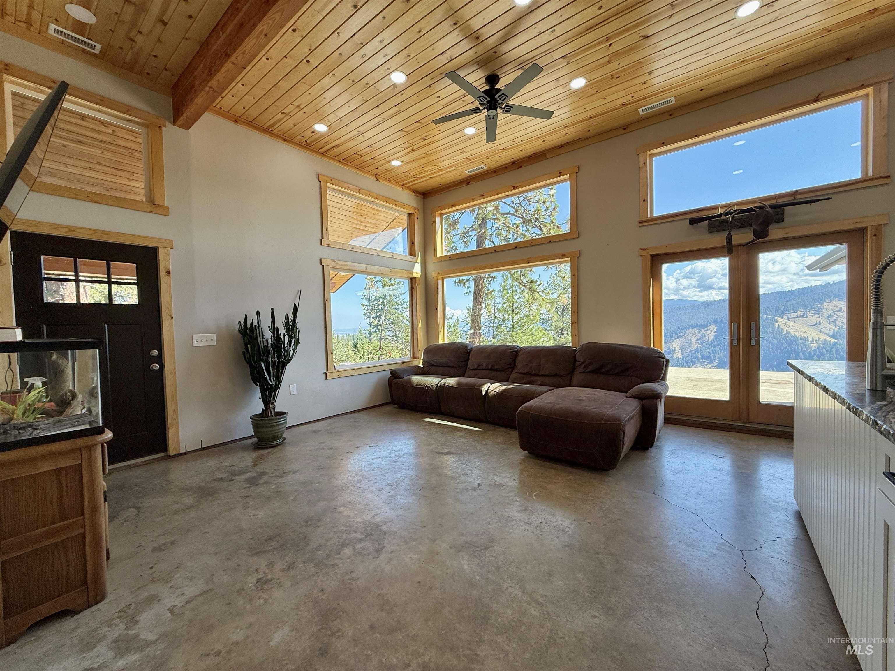 Living room with wooden ceiling, unfinished concrete flooring, plenty of natural light, a high ceiling, and a ceiling fan