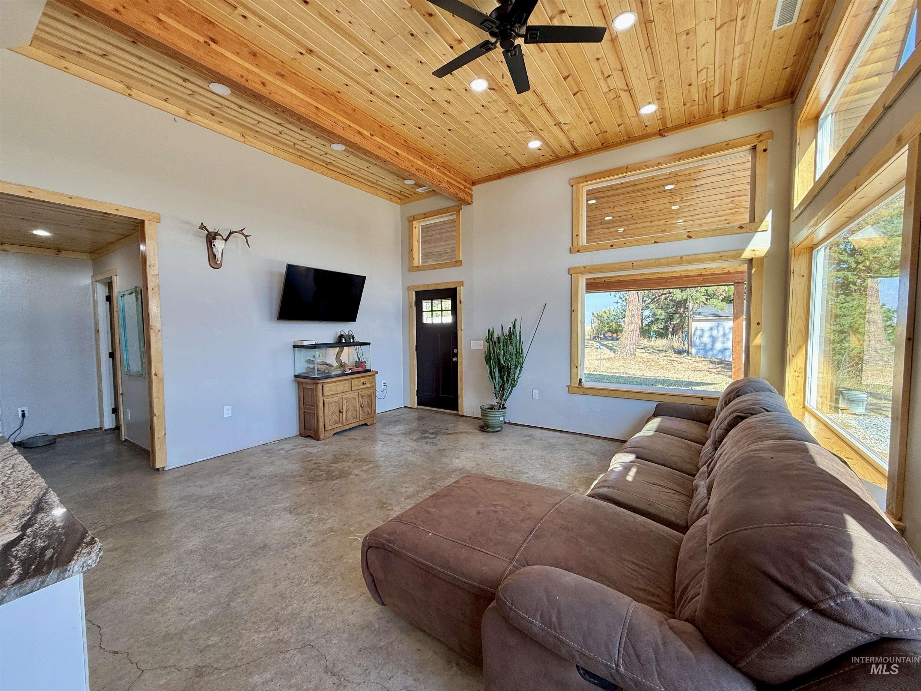 Living room with wooden ceiling, recessed lighting, concrete flooring, a ceiling fan, and a towering ceiling
