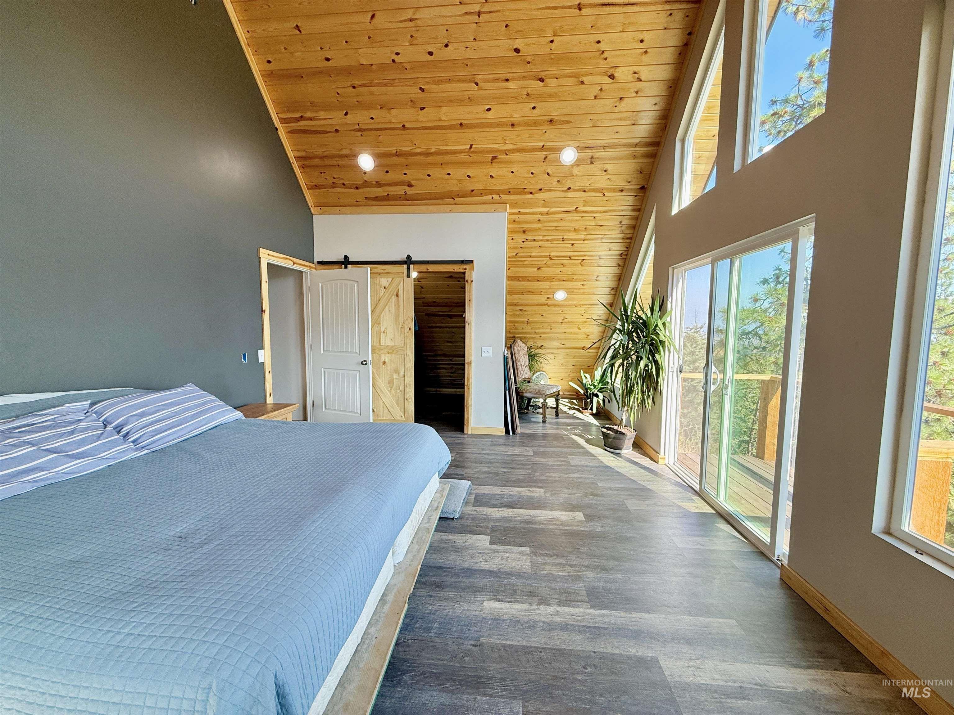 Bedroom with a barn door, high vaulted ceiling, wood ceiling, wood finished floors, and recessed lighting