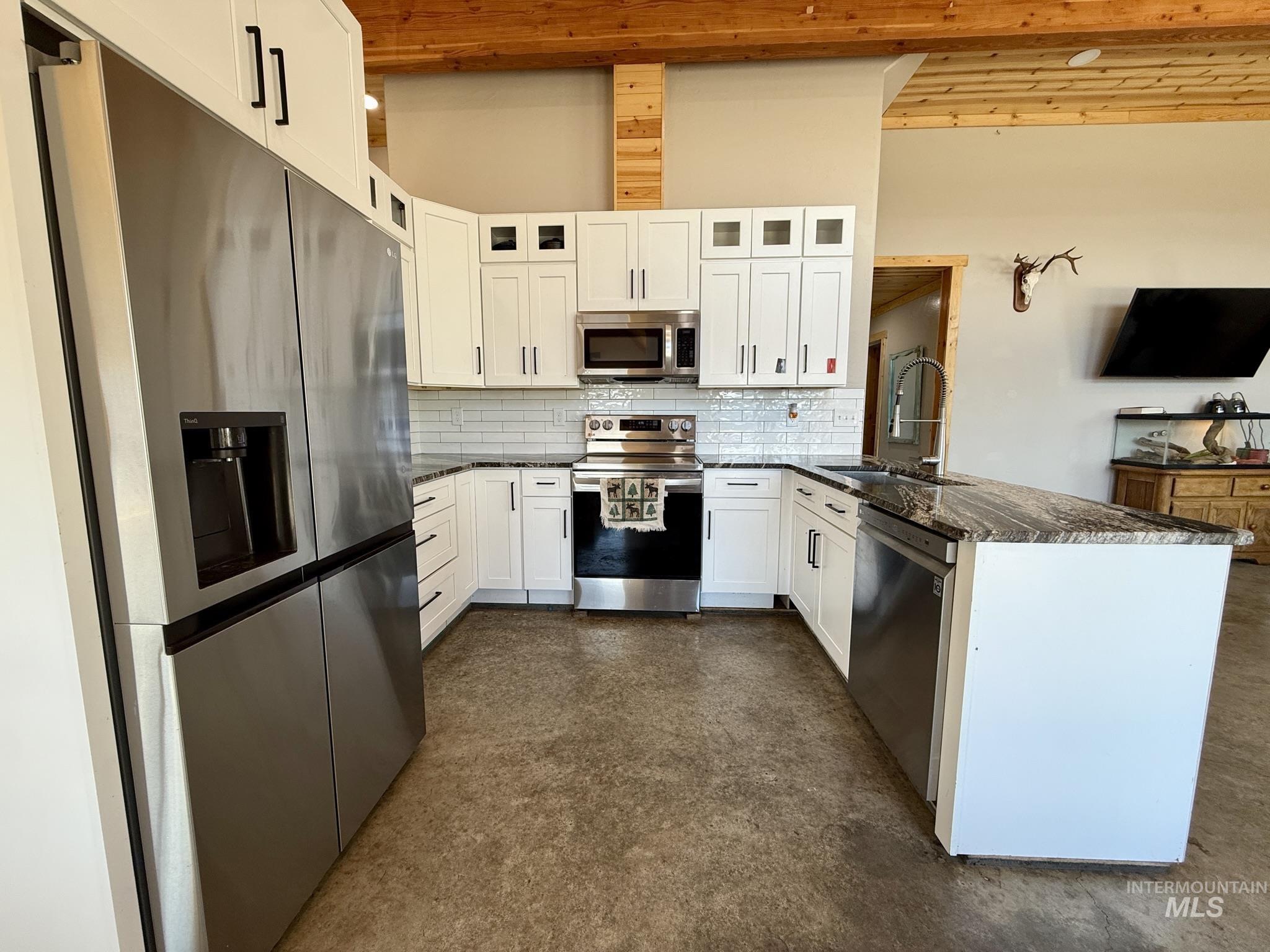 Kitchen with stainless steel appliances, a peninsula, backsplash, white cabinetry, and glass insert cabinets