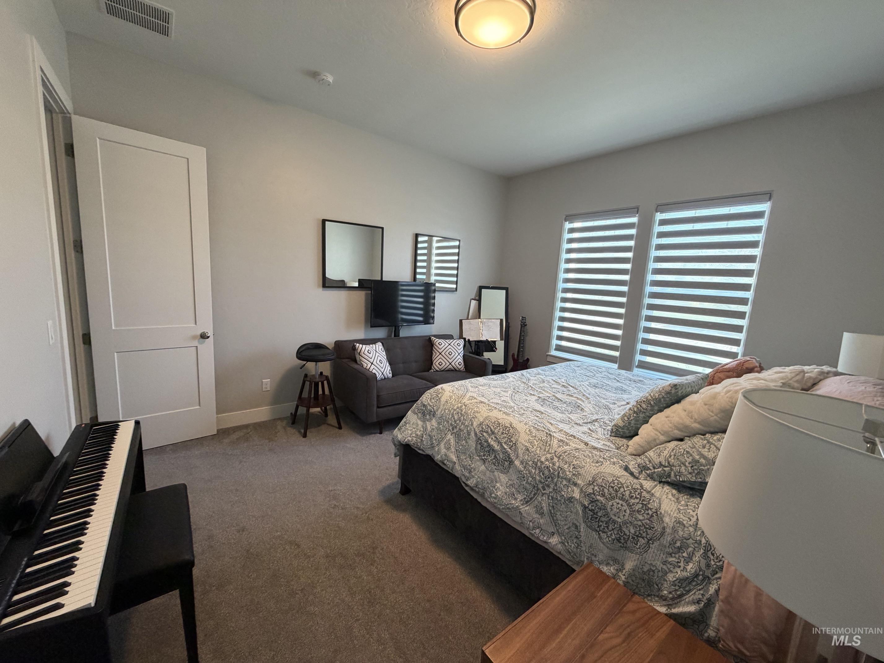 Spacious room featuring neutral carpeting, light gray wall tones, and two large windows with horizontal blinds