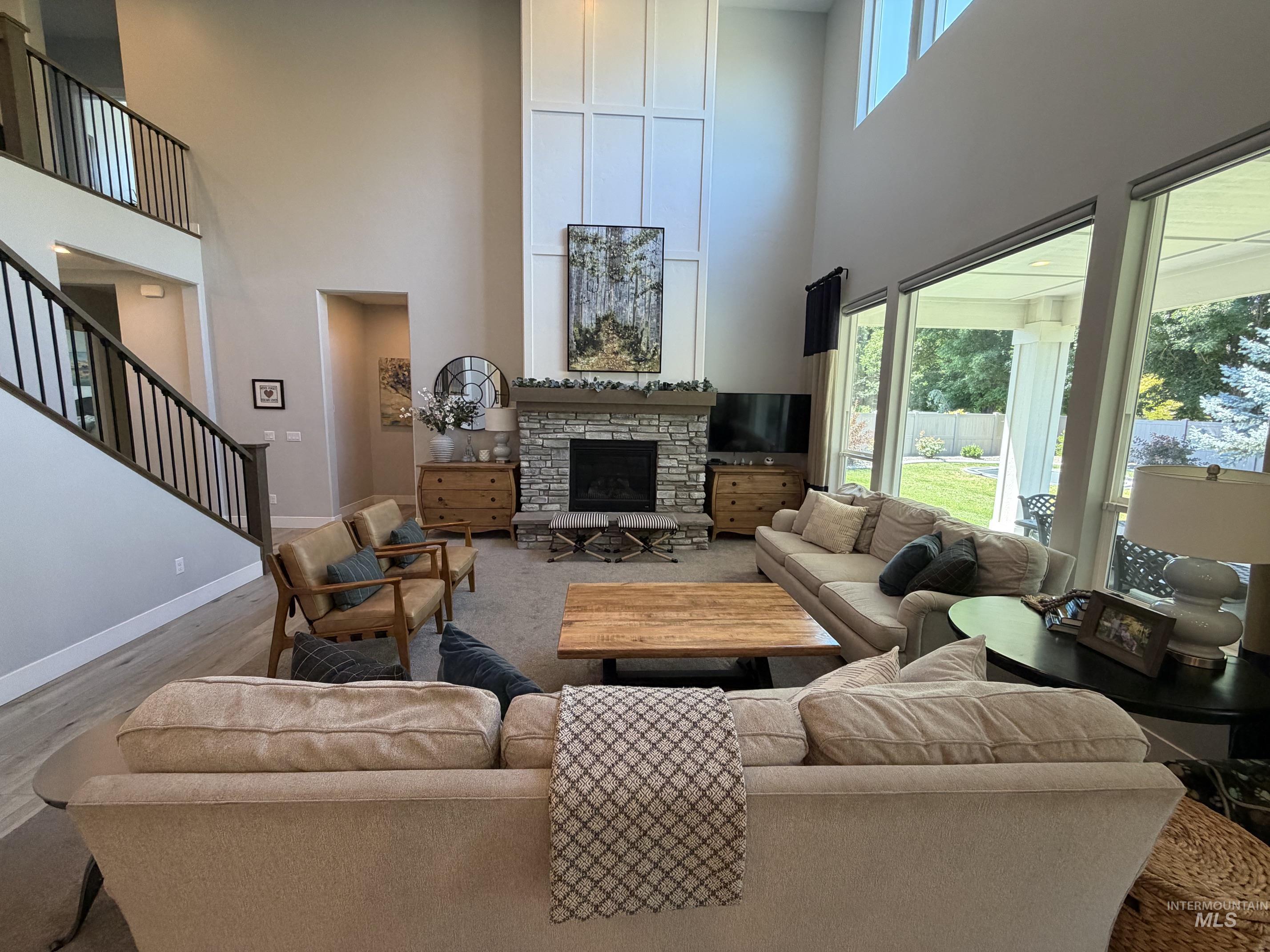 Living room featuring soaring ceilings, a stone-faced fireplace with a hearth, full-height board and batten detailing, a multi-story window wall, and light wood-finish flooring
