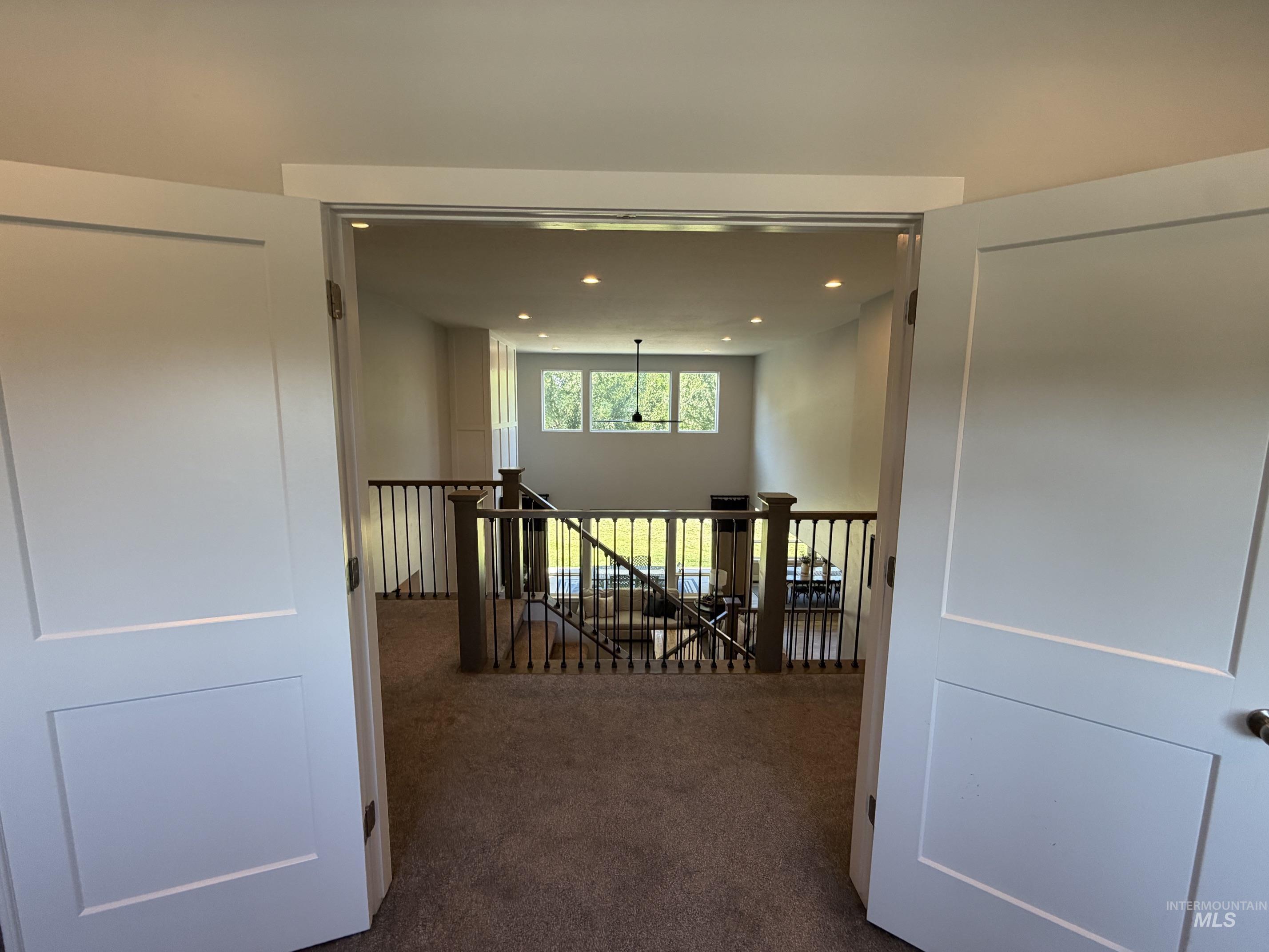 Open-concept upper level featuring a carpeted floor, white panel doors, recessed lighting, and a dark metal spindle railing system