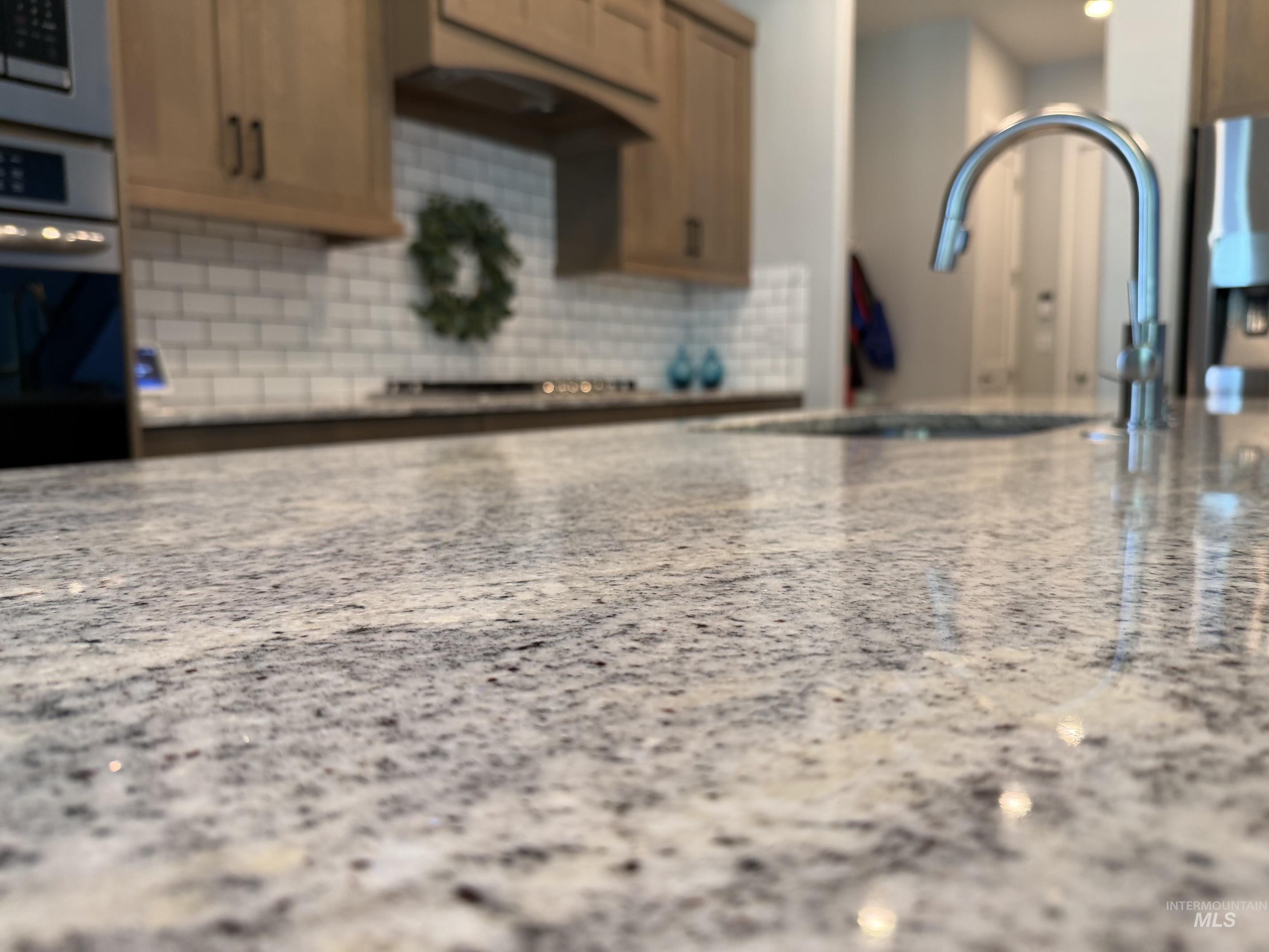 Kitchen island featuring a mottled stone countertop, undermount sink, and gooseneck faucet
