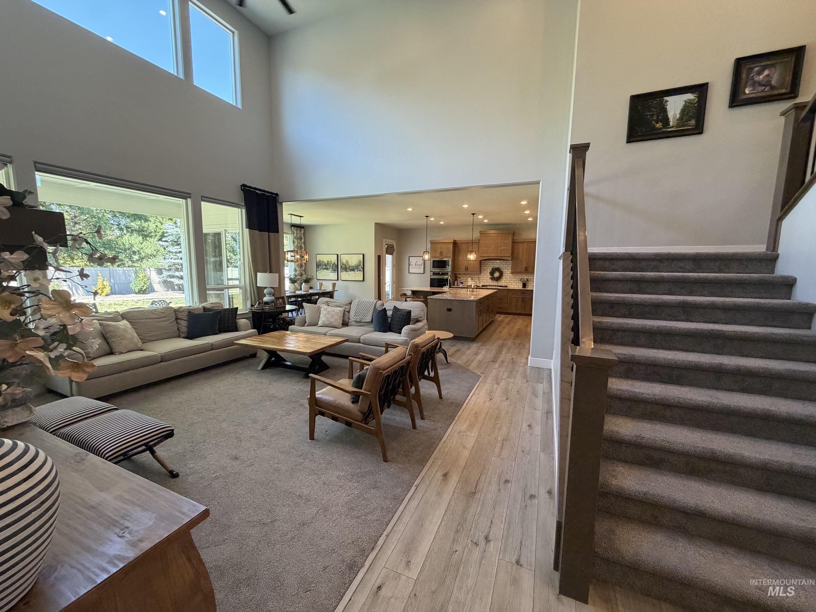 Open-concept living area featuring a two-story ceiling with high transom windows, expansive floor-to-ceiling windows, and wood-finish flooring