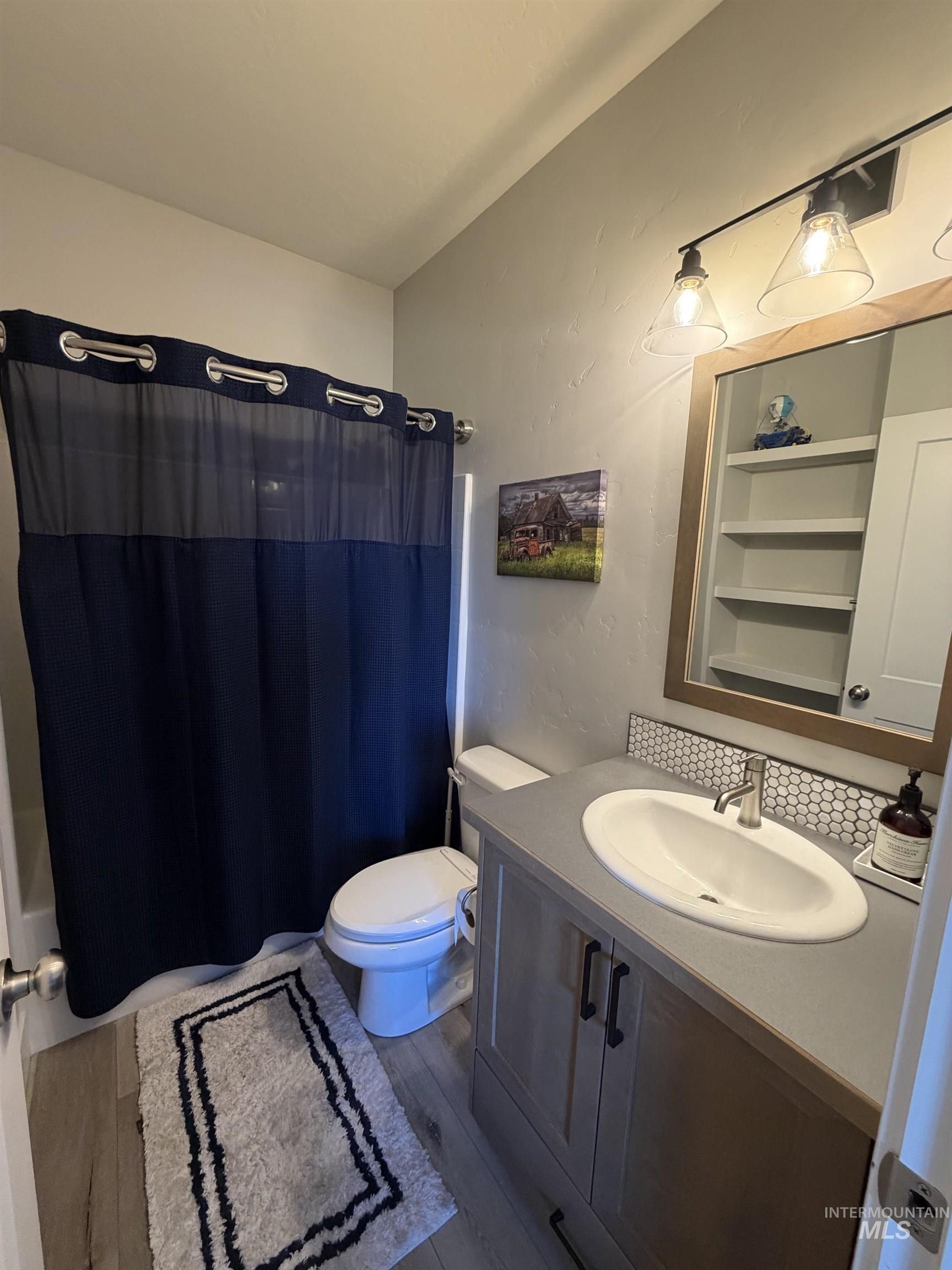 Bathroom featuring a light wood-finish vanity with a single basin sink, a gray countertop, and a honeycomb tile backsplash