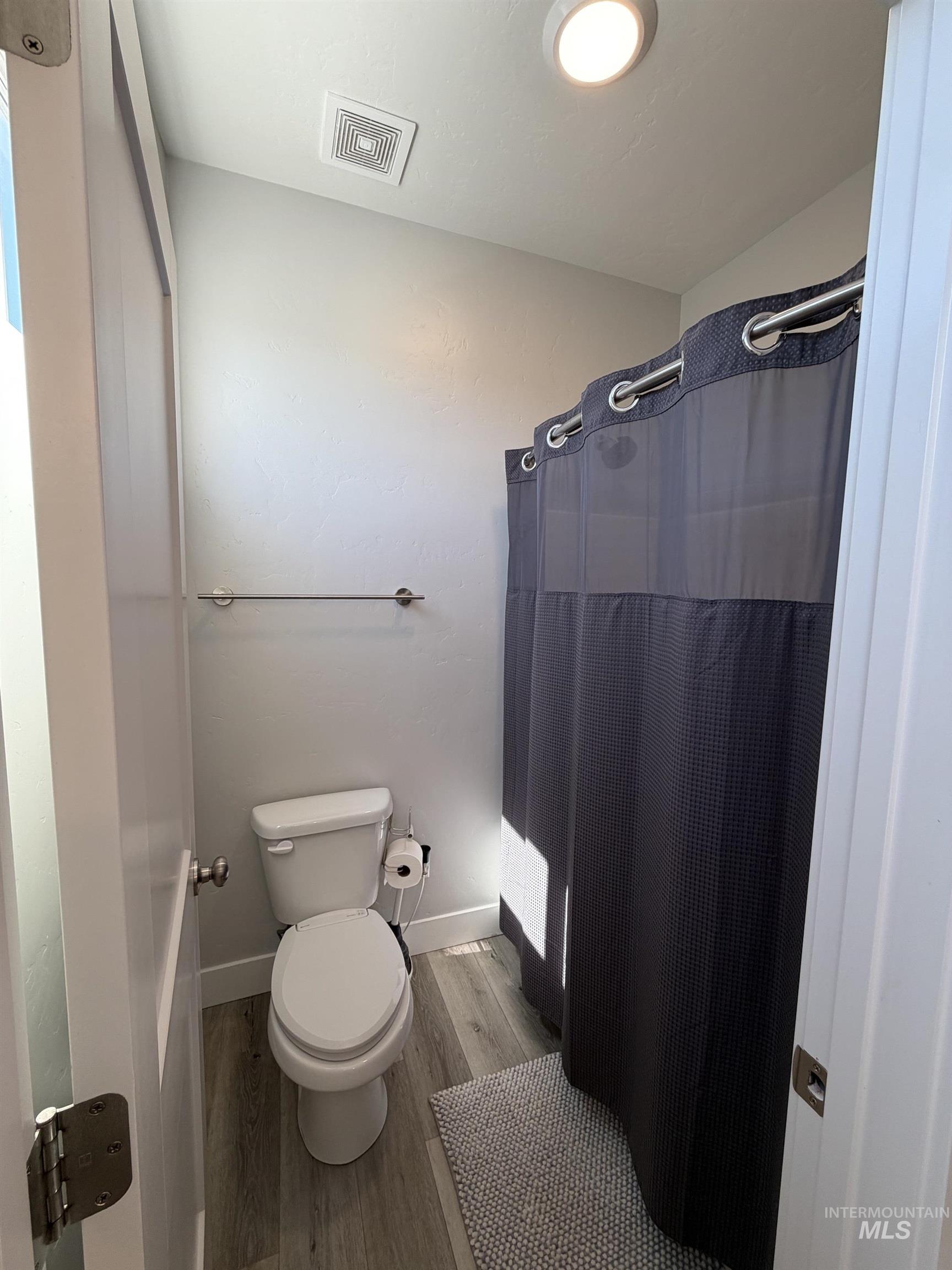 Full bathroom with light wood-finish flooring, a contemporary toilet, and a shower area featuring a dark privacy curtain