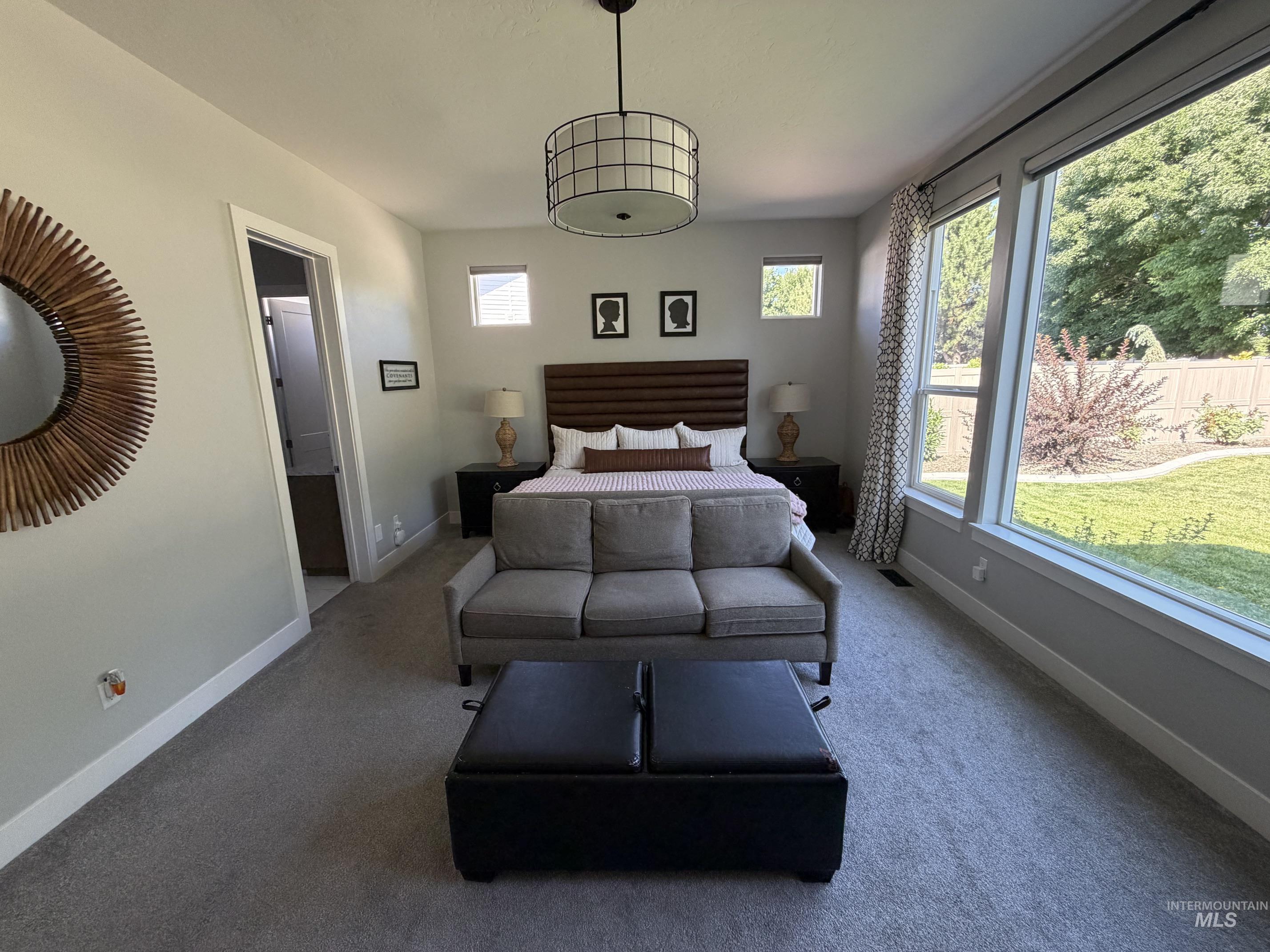Spacious room featuring broad windows with exterior views, carpet flooring, a contemporary drum pendant light fixture, and a wood-panel headboard