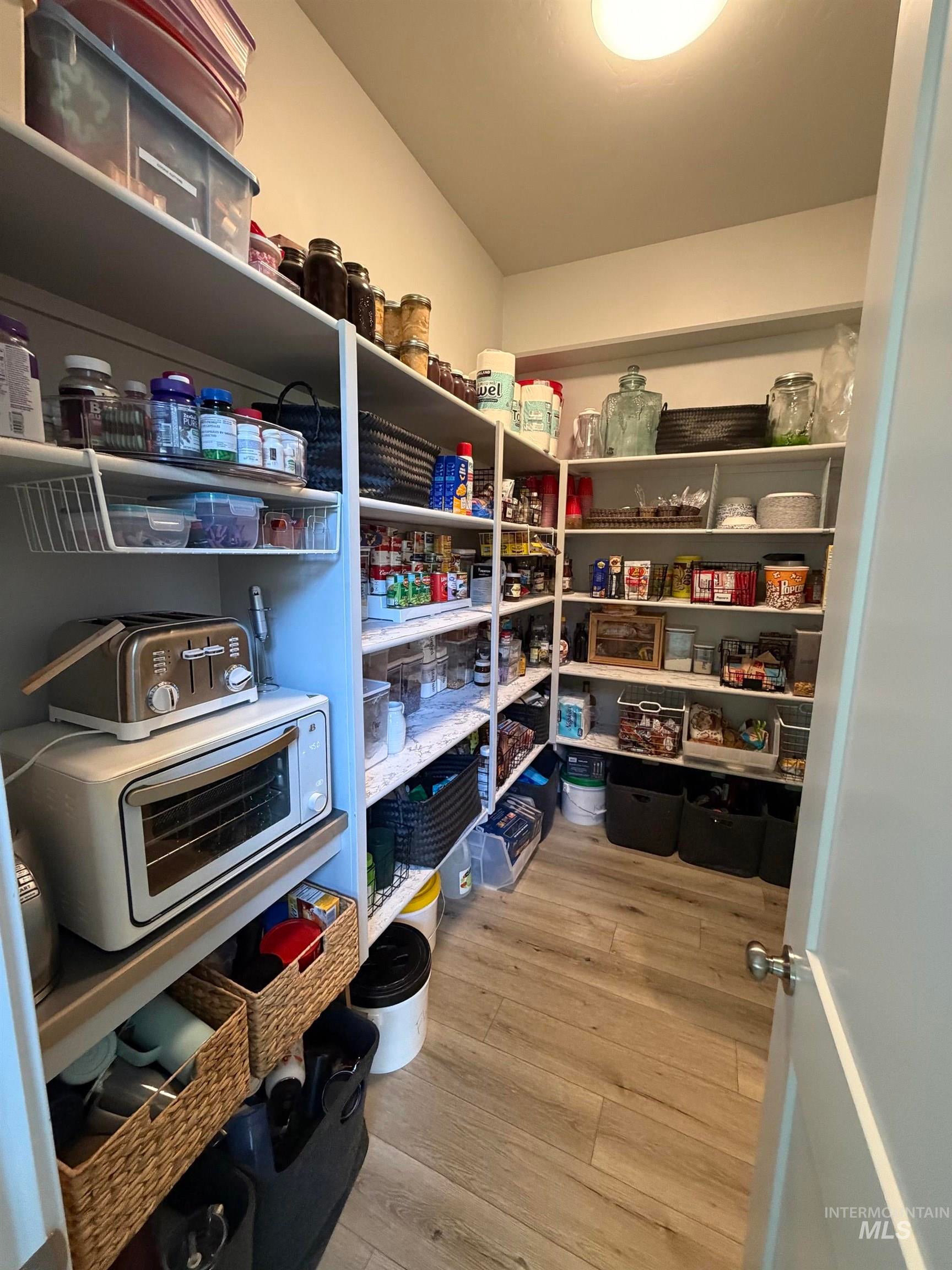 Spacious pantry featuring extensive built-in shelving, wood-finish flooring, and recessed overhead lighting