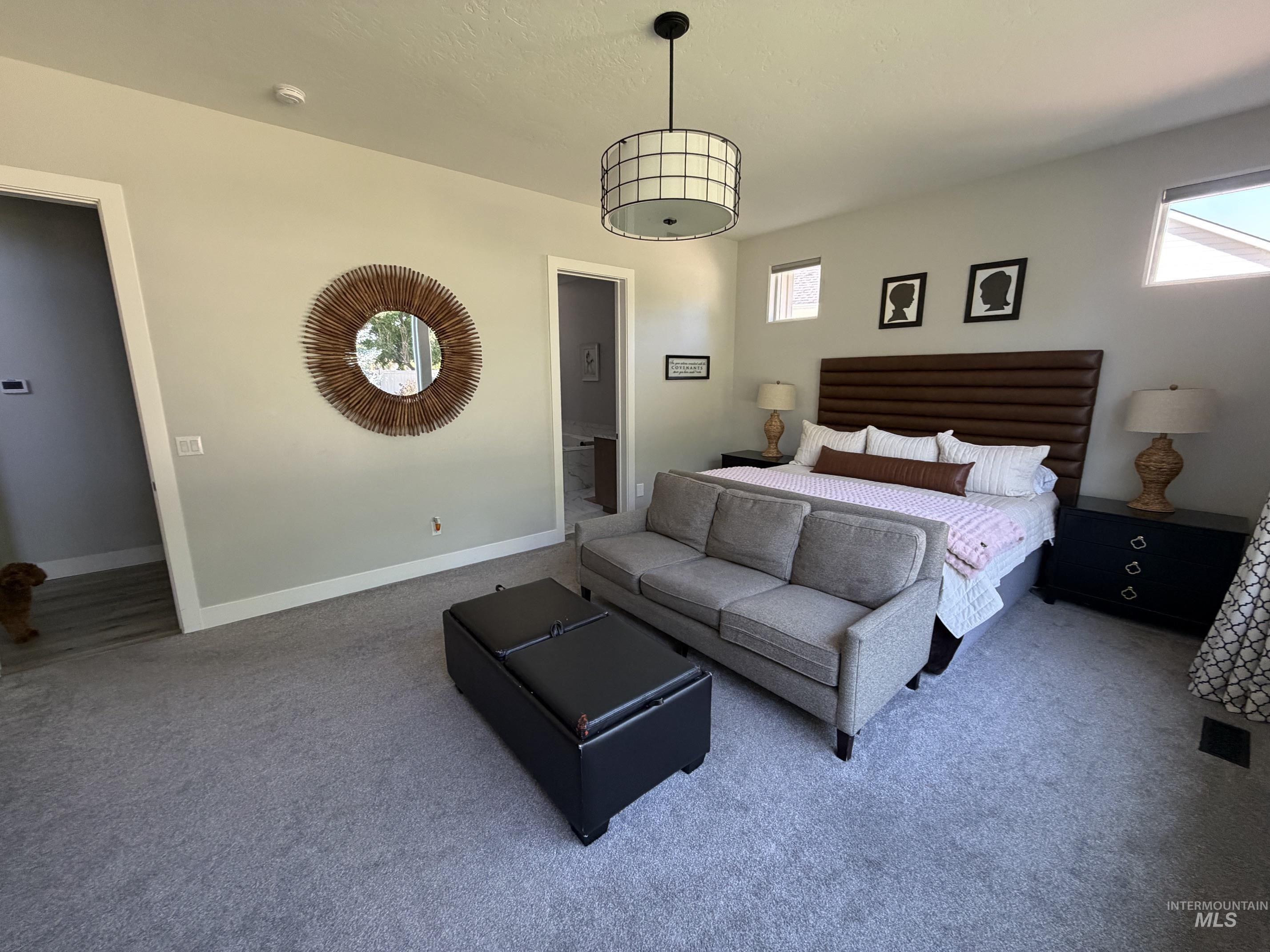 Spacious bedroom featuring light gray walls, carpet flooring, a contemporary drum pendant light, and multiple windows providing natural light