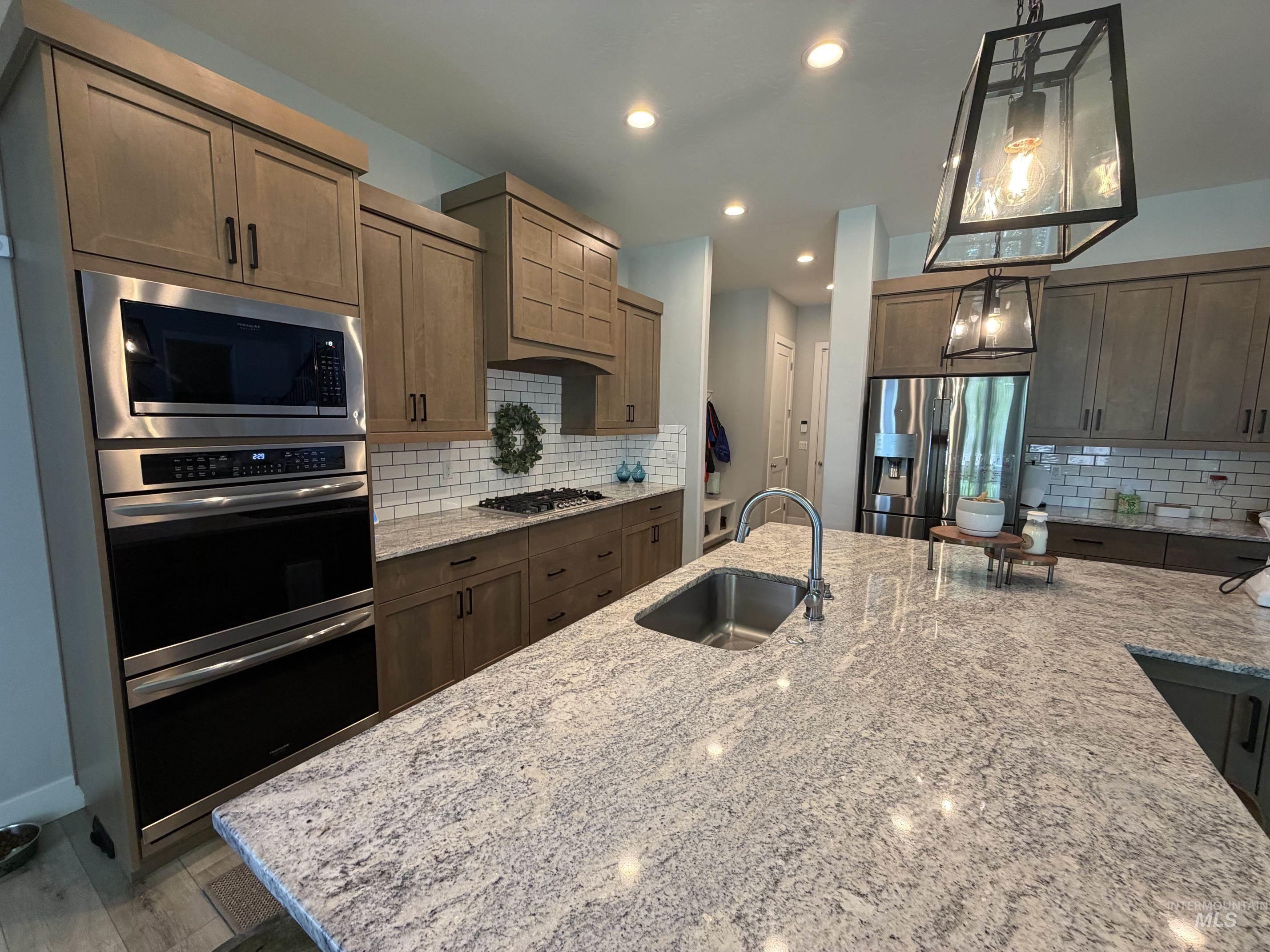 Spacious kitchen featuring a large island with an undermount sink, light-colored countertops, stainless steel appliances, wood-finish cabinetry, and subway tile backsplash