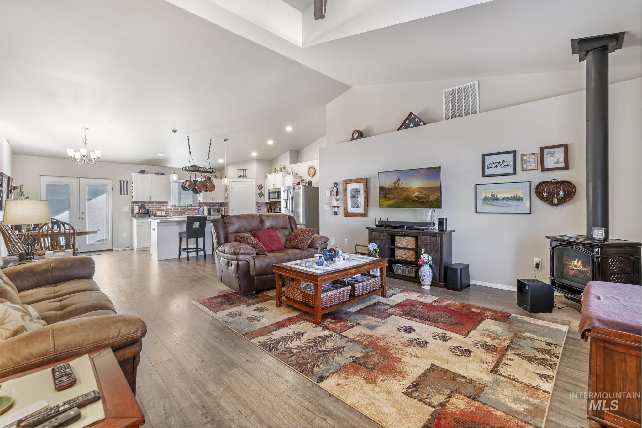 Living room featuring a wood stove, light wood-style flooring, a chandelier, recessed lighting, and high vaulted ceiling