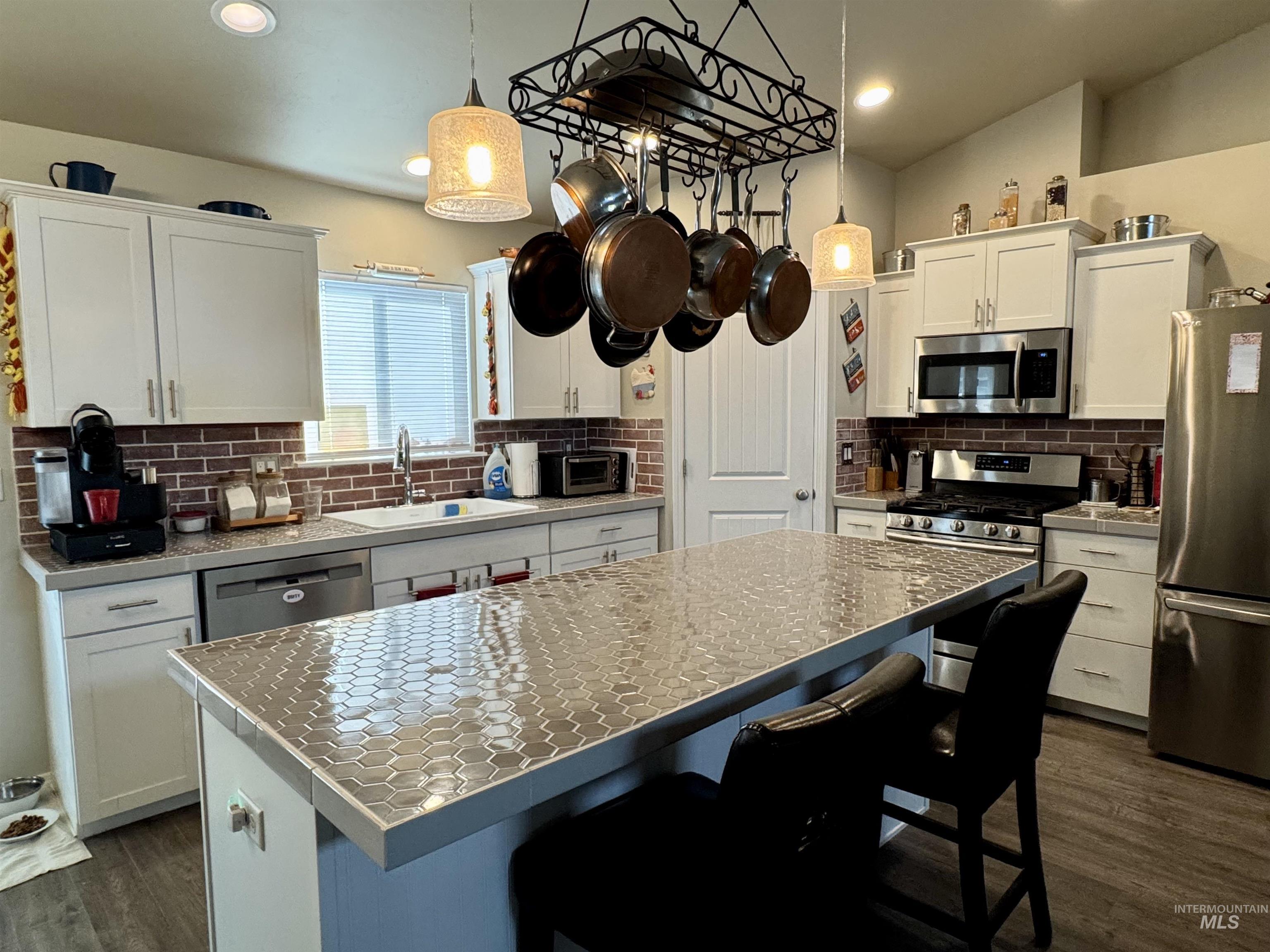 Kitchen with a kitchen breakfast bar, stainless steel appliances, a center island, white cabinets, and dark wood-style floors
