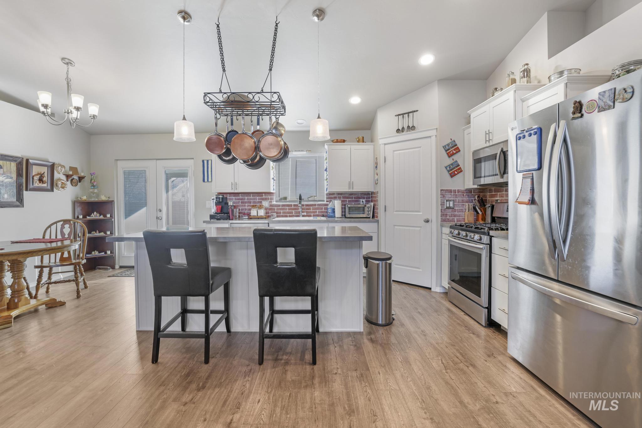 Kitchen featuring appliances with stainless steel finishes, a kitchen island, white cabinetry, hanging light fixtures, and decorative backsplash