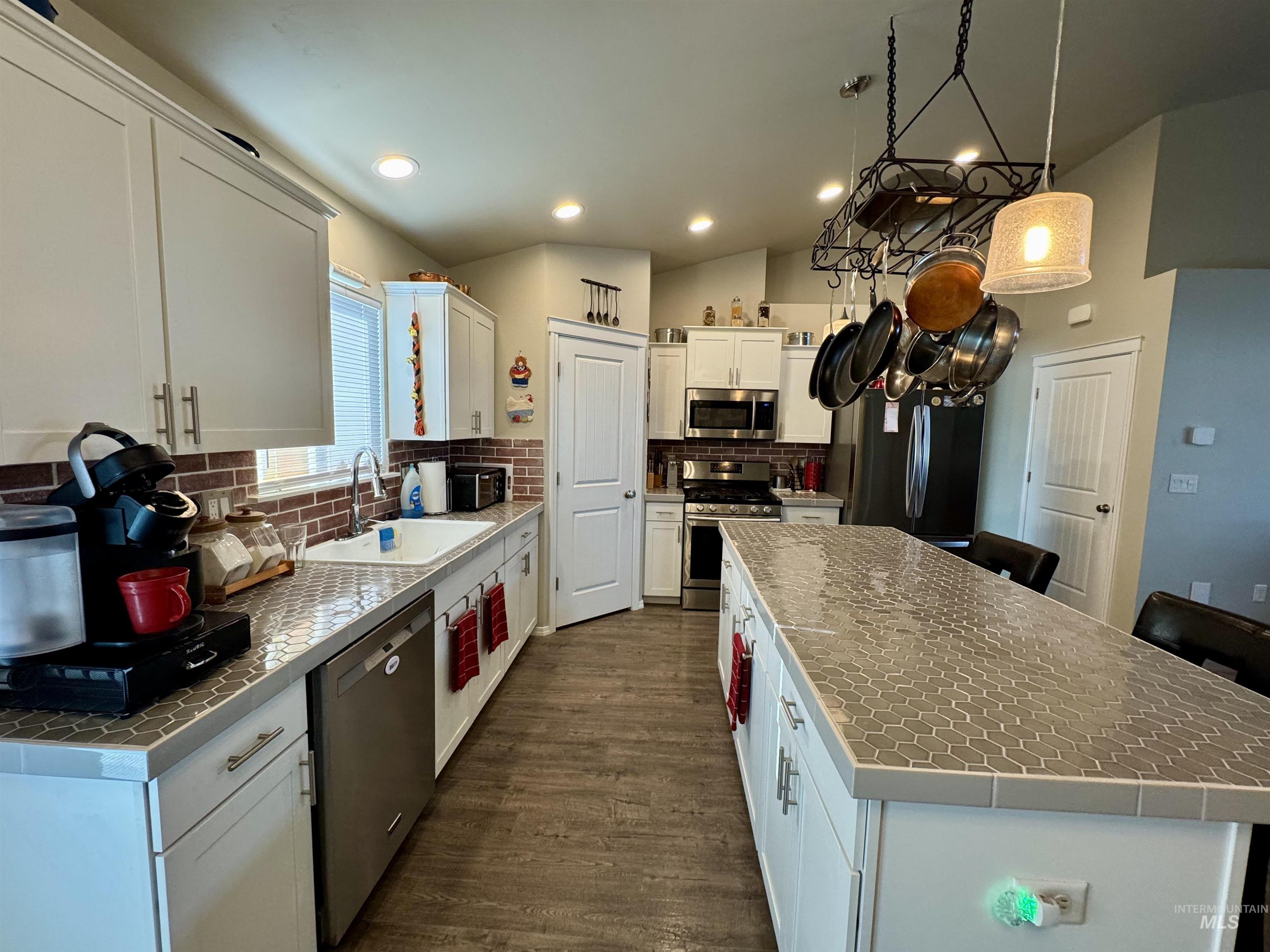 Kitchen with tile counters, stainless steel appliances, white cabinets, tasteful backsplash, and vaulted ceiling