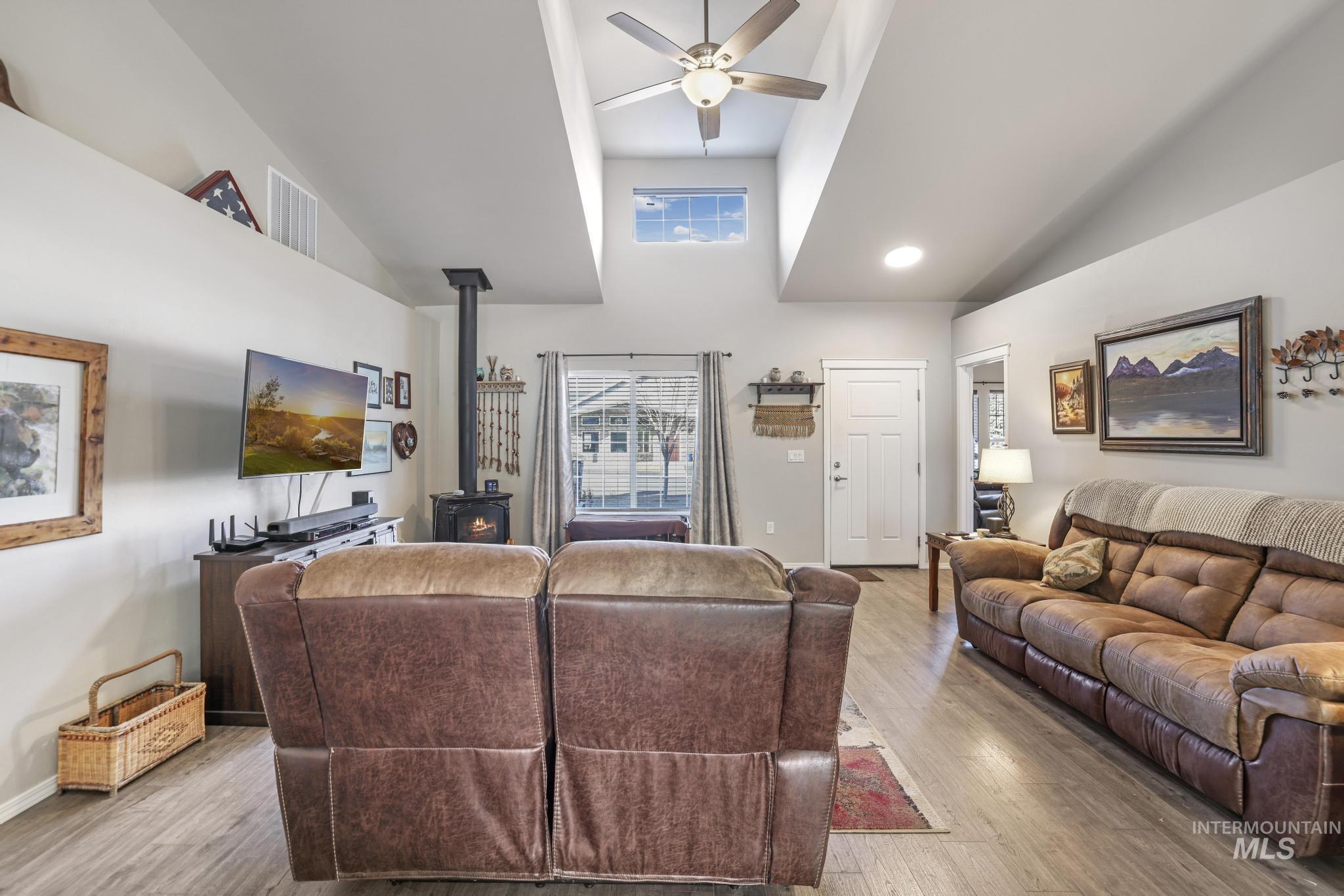 Living room featuring a wood stove, light wood finished floors, high vaulted ceiling, and ceiling fan