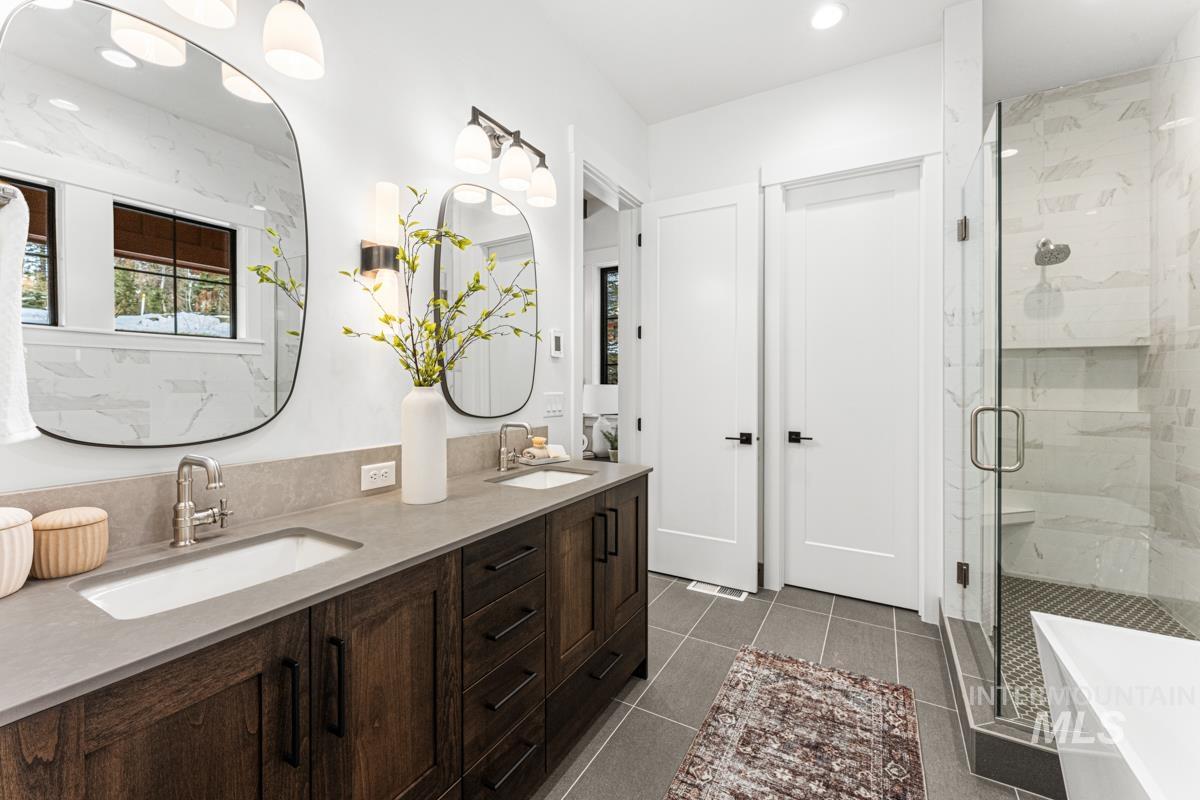 Full bath featuring double vanity, a marble finish shower, a freestanding bath, dark tile patterned flooring, and recessed lighting