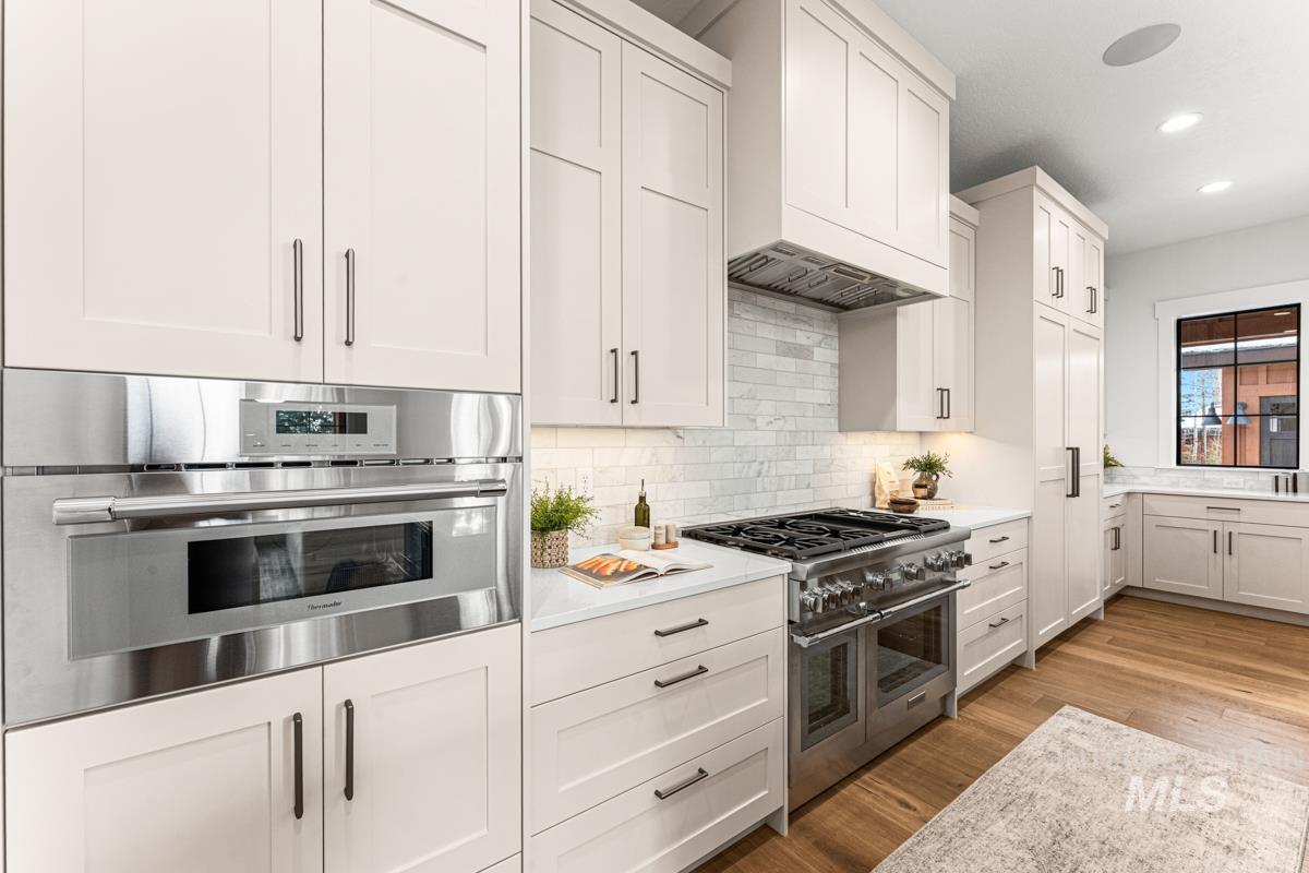 Kitchen featuring appliances with stainless steel finishes, white cabinets, light wood-style floors, tasteful backsplash, and custom range hood