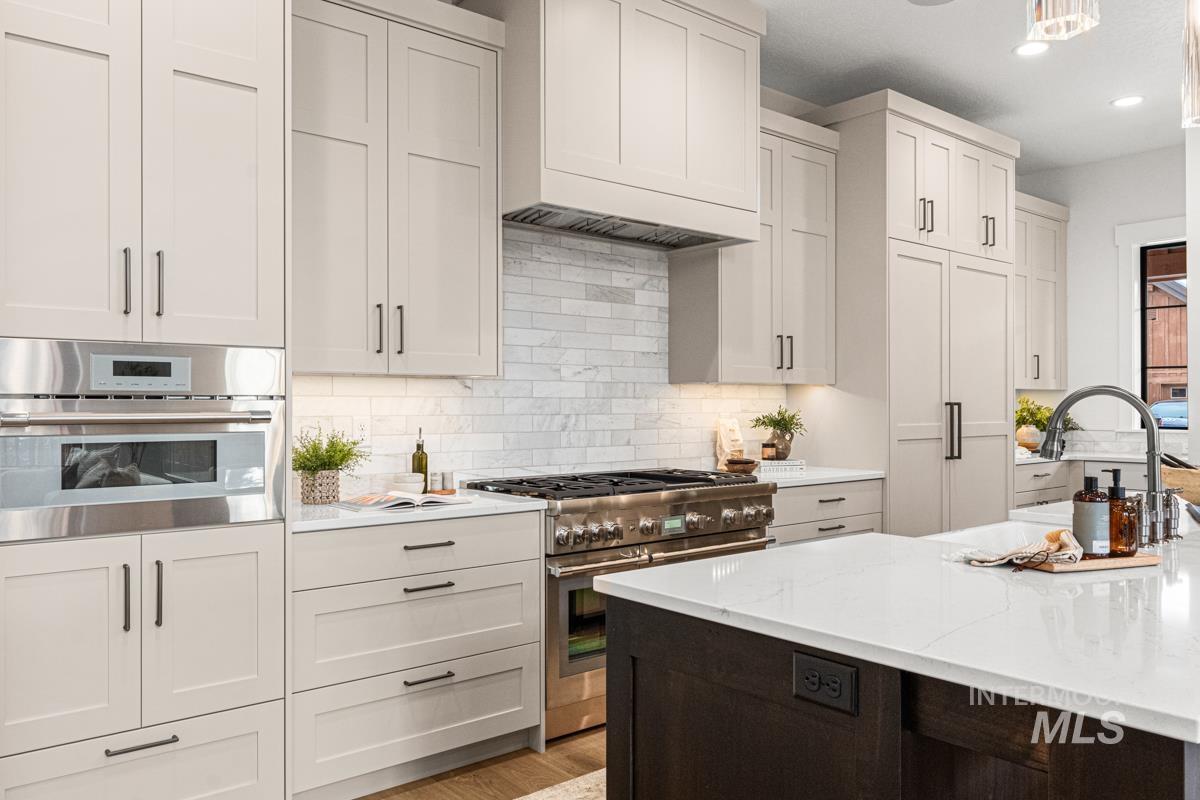 Kitchen featuring stainless steel appliances, tasteful backsplash, custom exhaust hood, white cabinets, and light stone countertops
