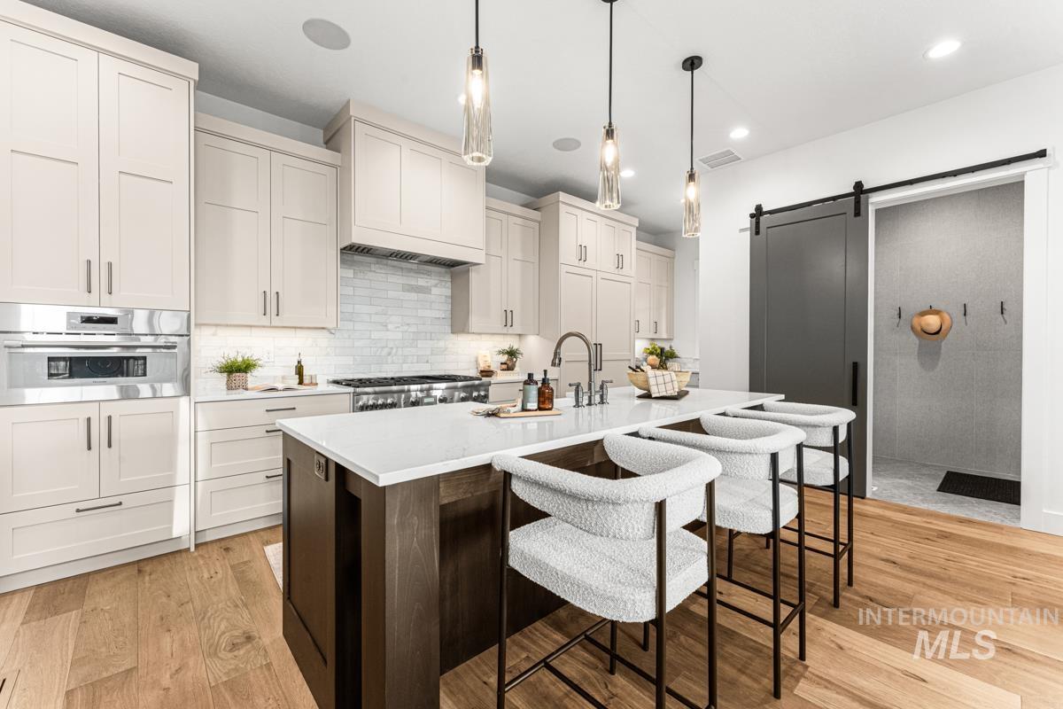 Kitchen with a kitchen breakfast bar, light wood-type flooring, dark brown cabinetry, a barn door, and pendant lighting
