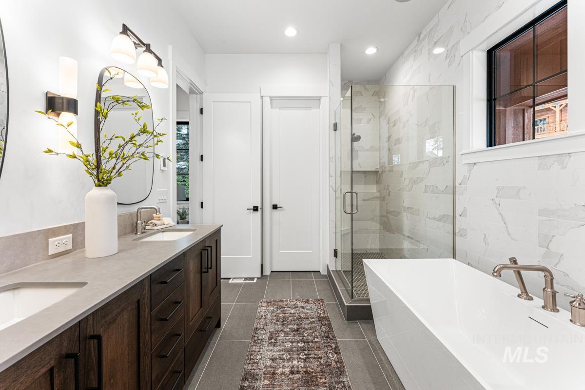 Full bath with double vanity, a soaking tub, a marble finish shower, recessed lighting, and dark tile patterned floors
