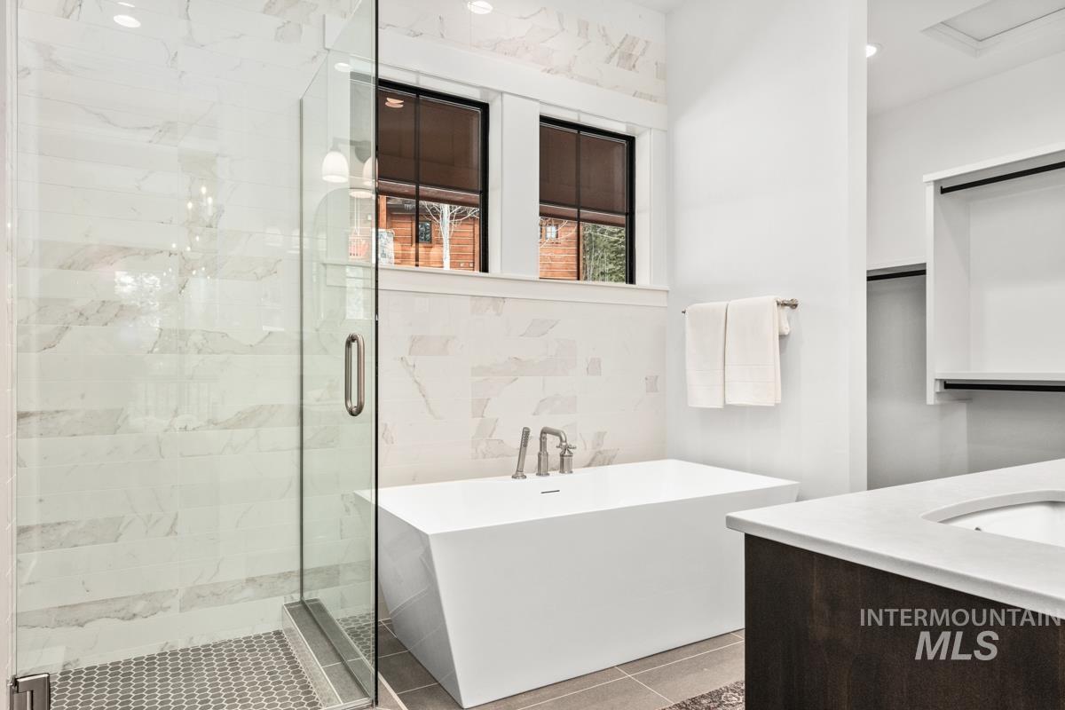Full bath featuring vanity, a stall shower, a freestanding tub, tile walls, and tile patterned floors