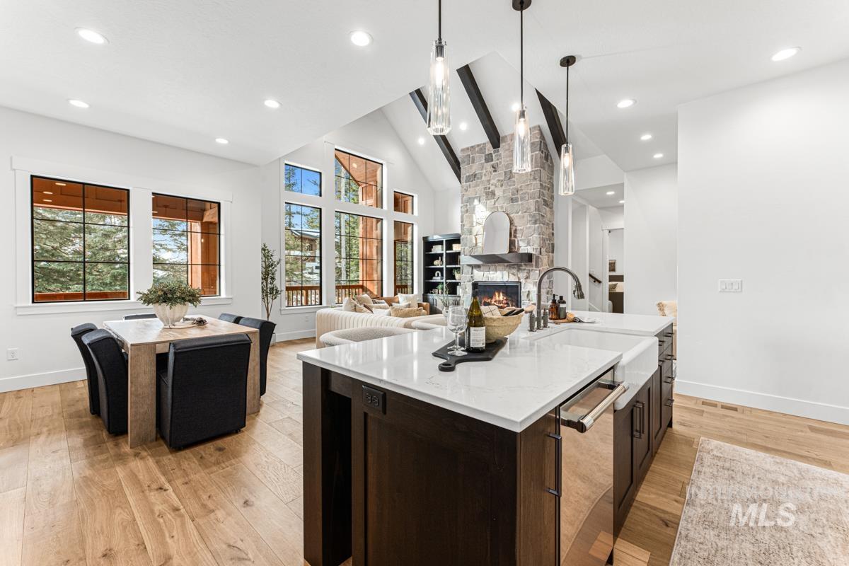Kitchen featuring dark brown cabinets, high vaulted ceiling, a fireplace, an island with sink, and light wood-style floors