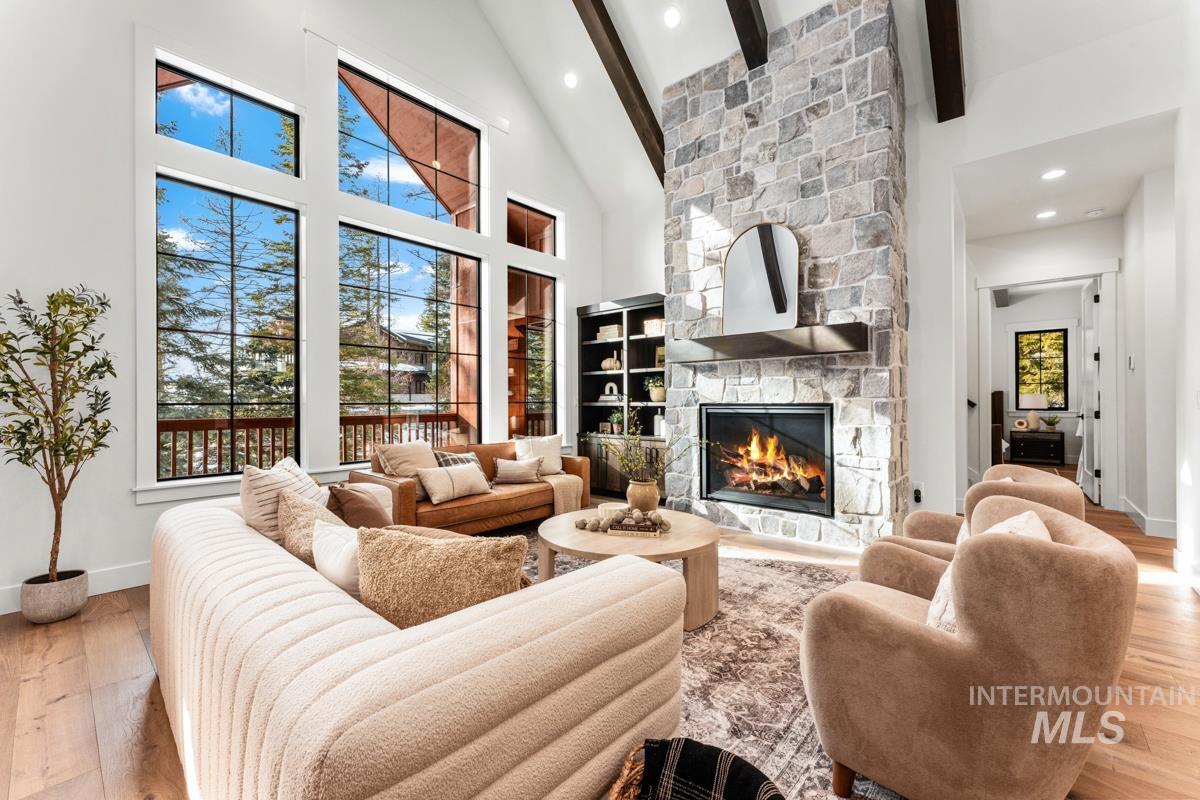 Living room featuring light wood-style flooring, a stone fireplace, beam ceiling, recessed lighting, and high vaulted ceiling