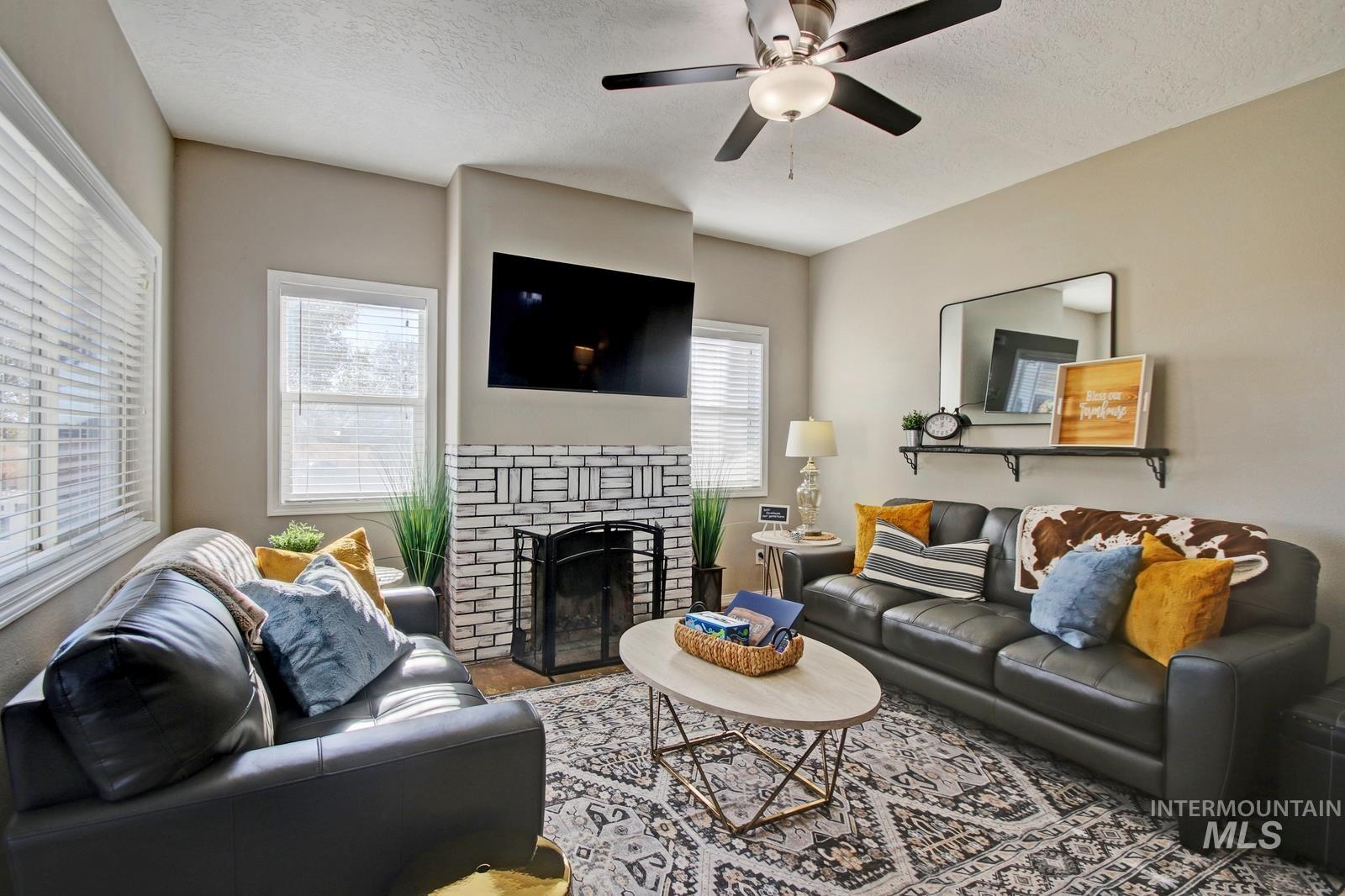 Living area featuring a brick fireplace, a textured ceiling, and ceiling fan