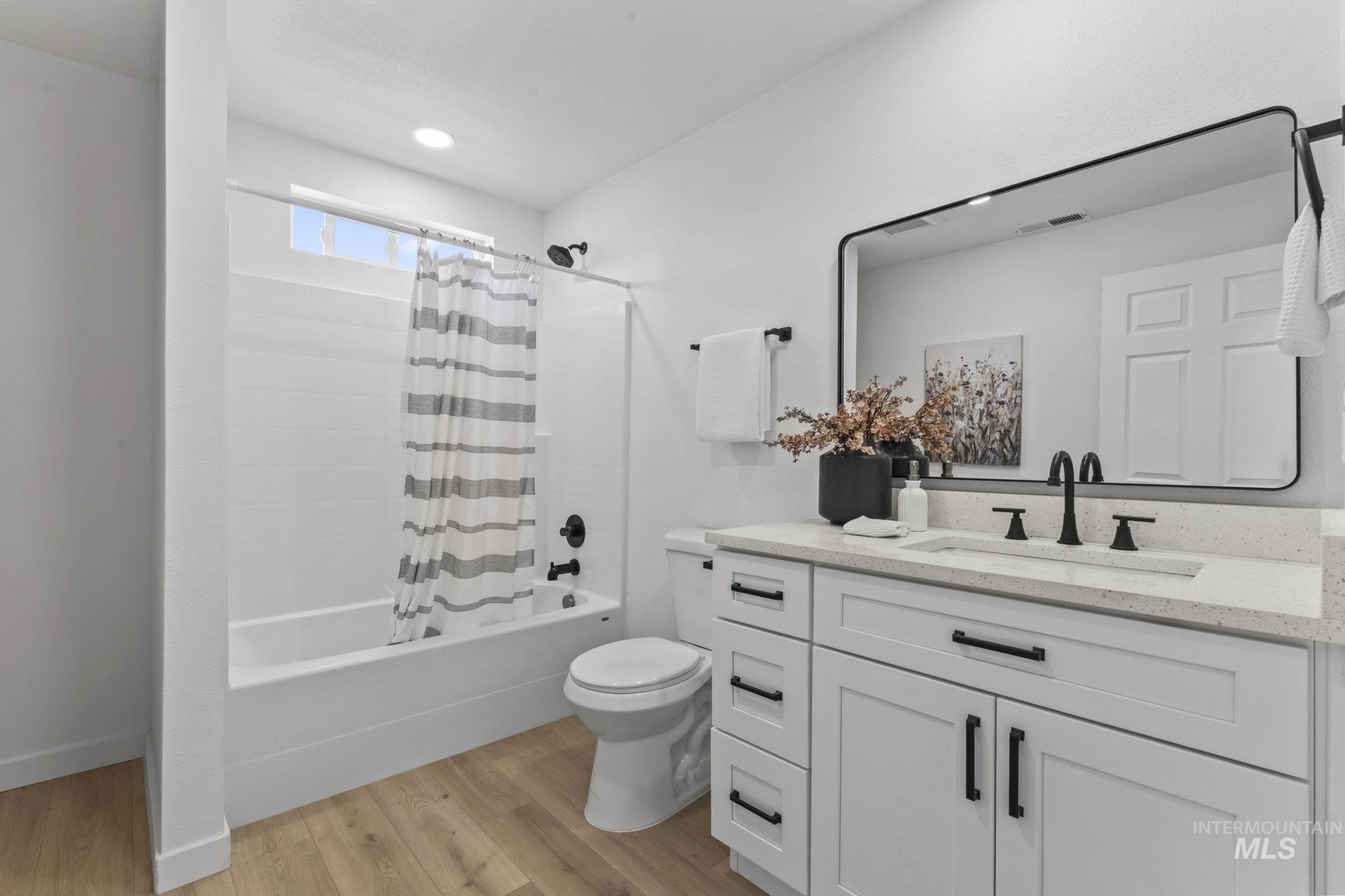 Full bathroom featuring vanity, wood finished floors, shower / bathtub combination with curtain, and recessed lighting