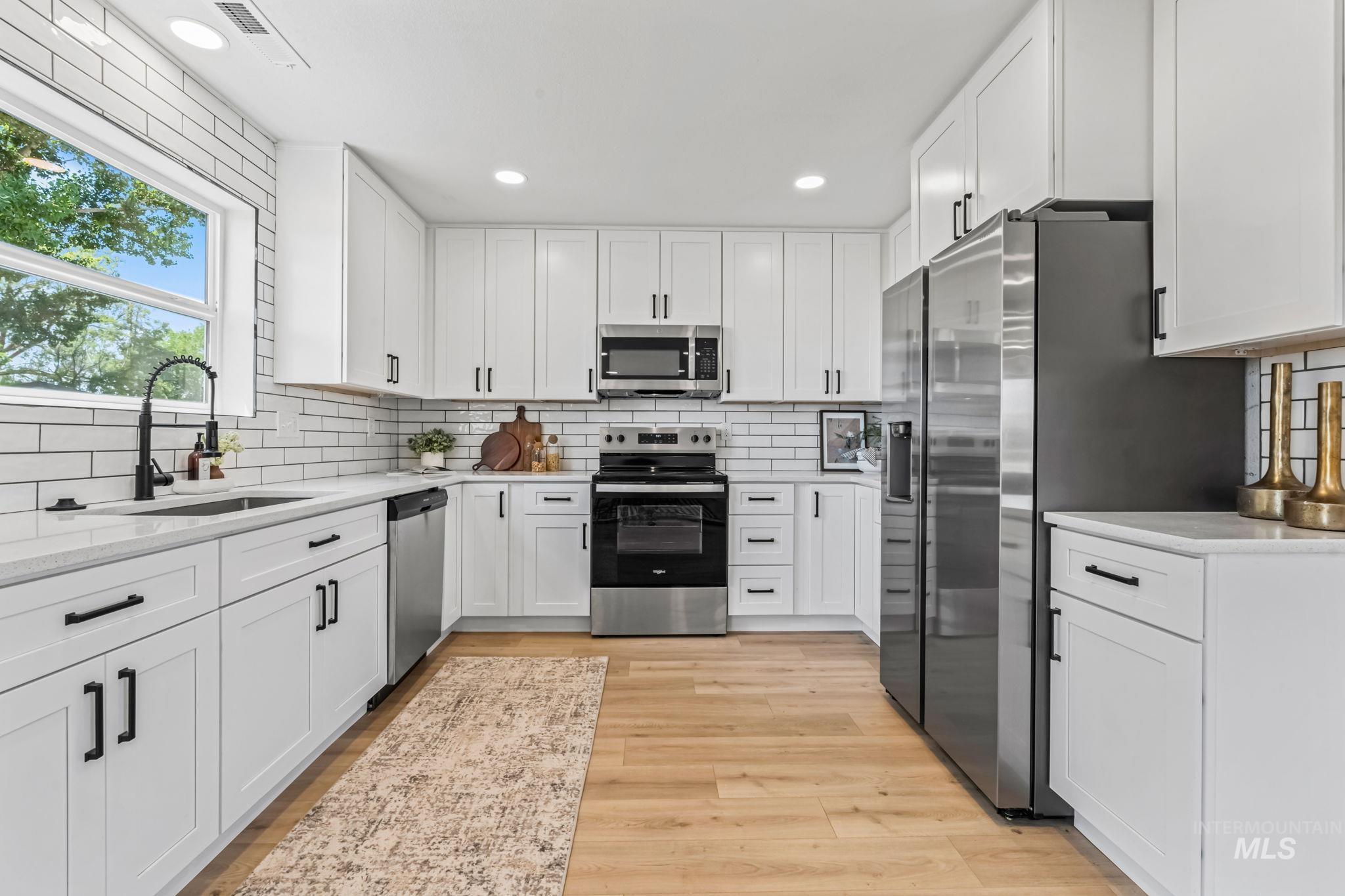 Kitchen featuring tasteful backsplash, appliances with stainless steel finishes, white cabinets, recessed lighting, and light wood-style floors