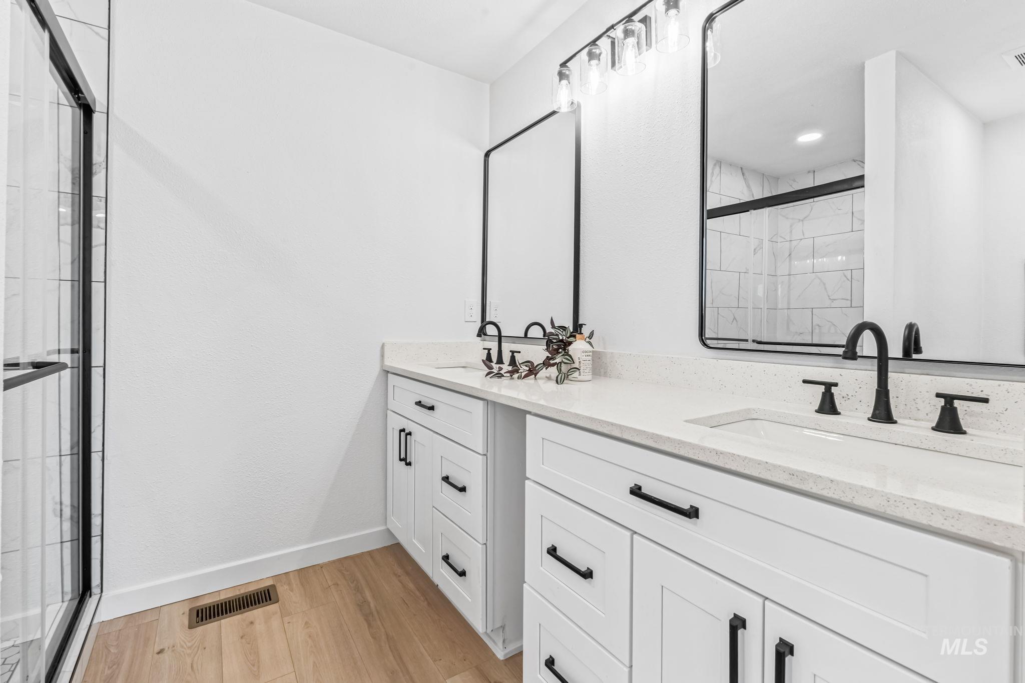 Full bathroom featuring wood finished floors, double vanity, and a tile shower