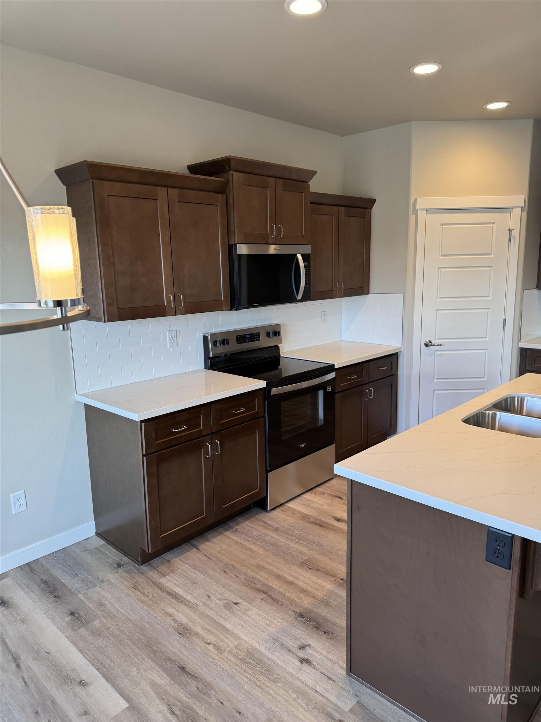 Kitchen featuring decorative backsplash, stainless steel appliances, dark wood finish cabinetry, light wood-style flooring, and recessed lighting