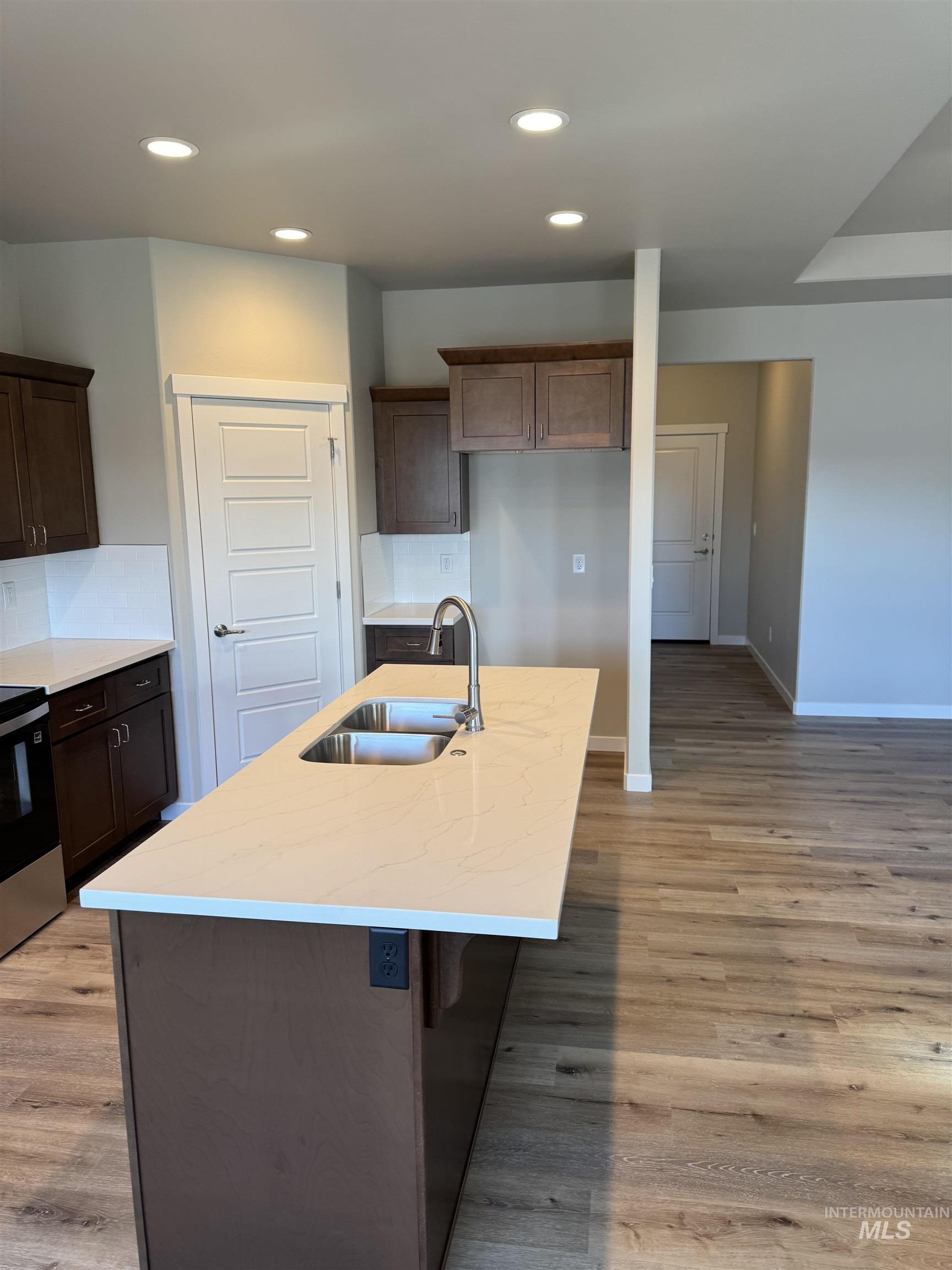 Kitchen featuring light stone counters, stainless steel electric range oven, a center island with sink, a kitchen bar, and light wood-type flooring