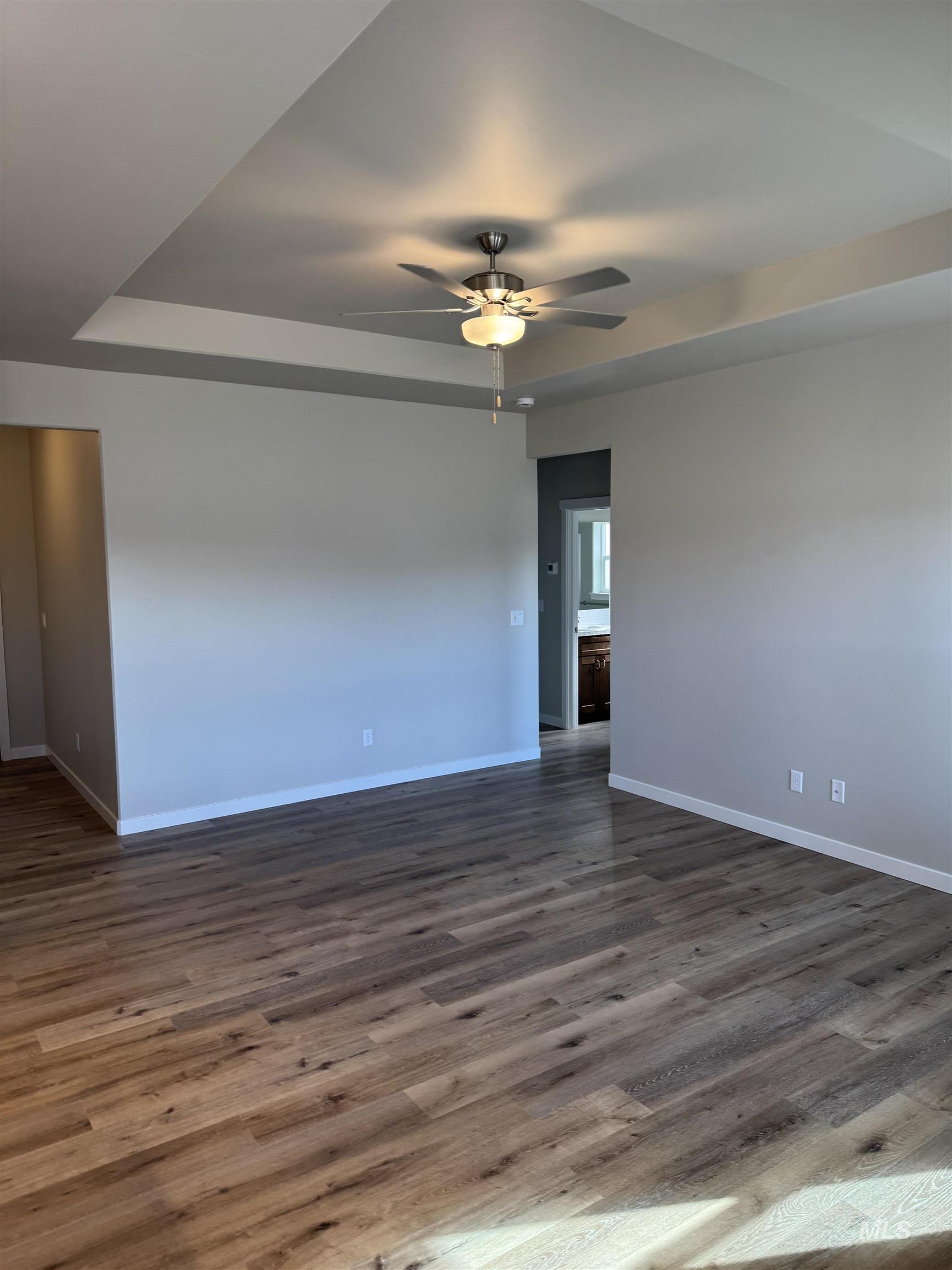 Empty room with a tray ceiling, a ceiling fan, and dark wood-type flooring