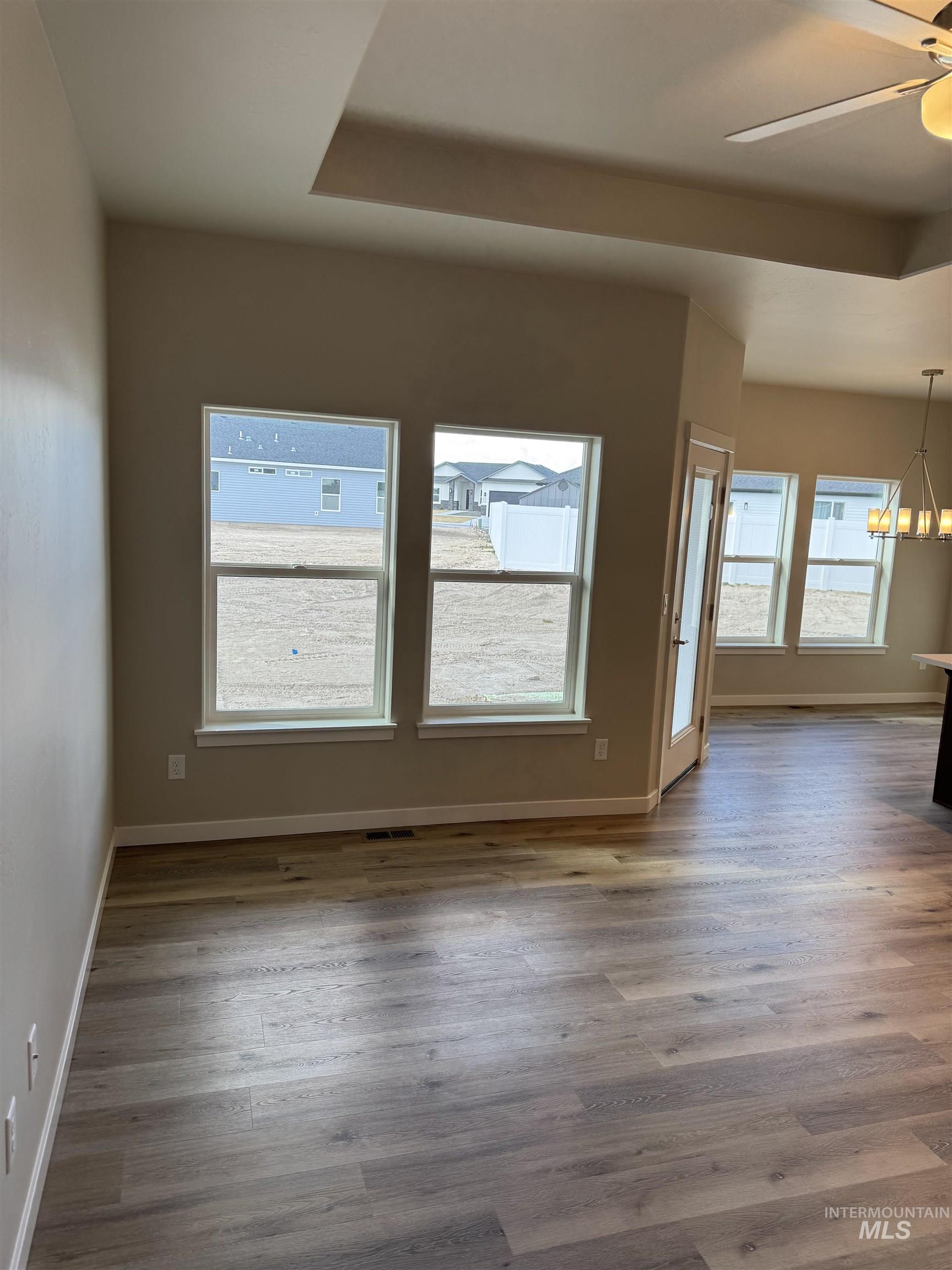 Spare room with ceiling fan, light wood-type flooring, healthy amount of natural light, and suspended lighting