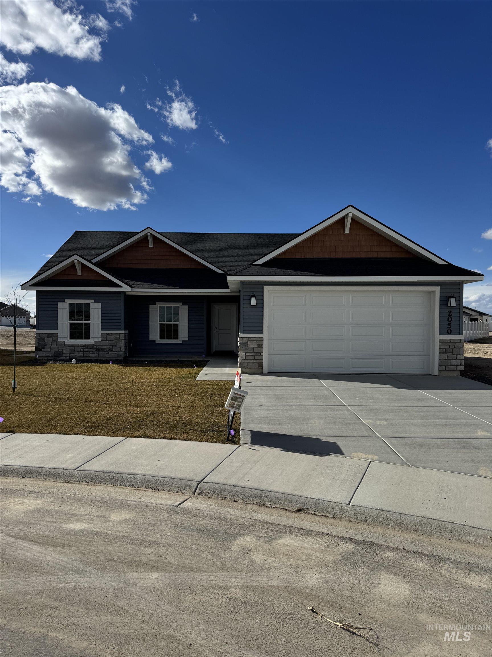 View of front of house with stone siding, driveway, a front yard, and an attached garage