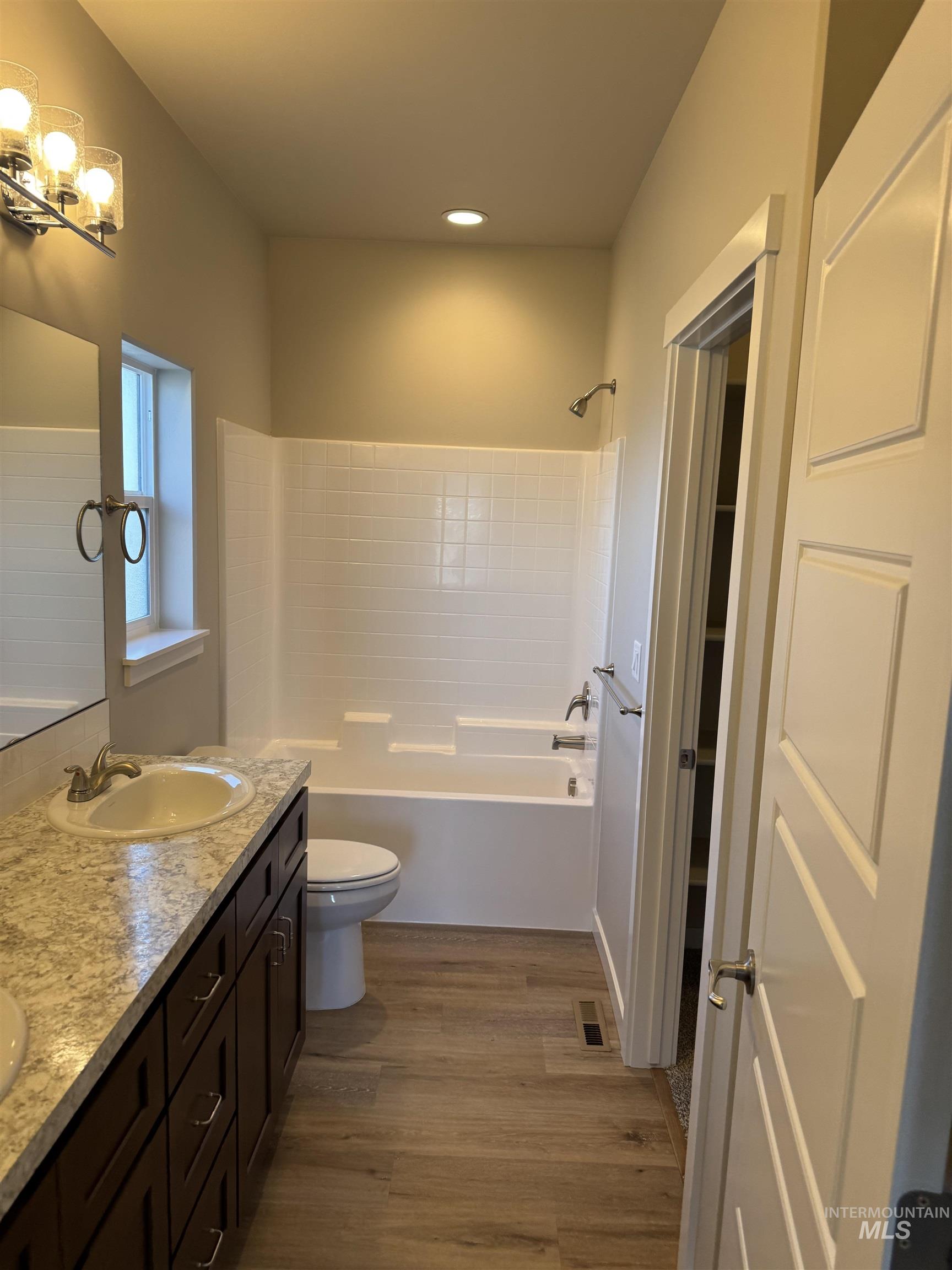 Full bath with double vanity, shower / bathtub combination, light wood finished floors, and recessed lighting
