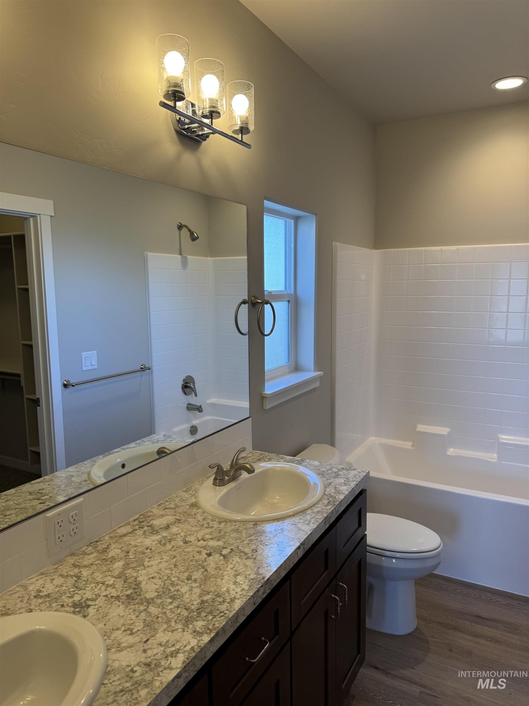 Full bath with washtub / shower combination, double vanity, dark wood-style flooring, and a walk in closet