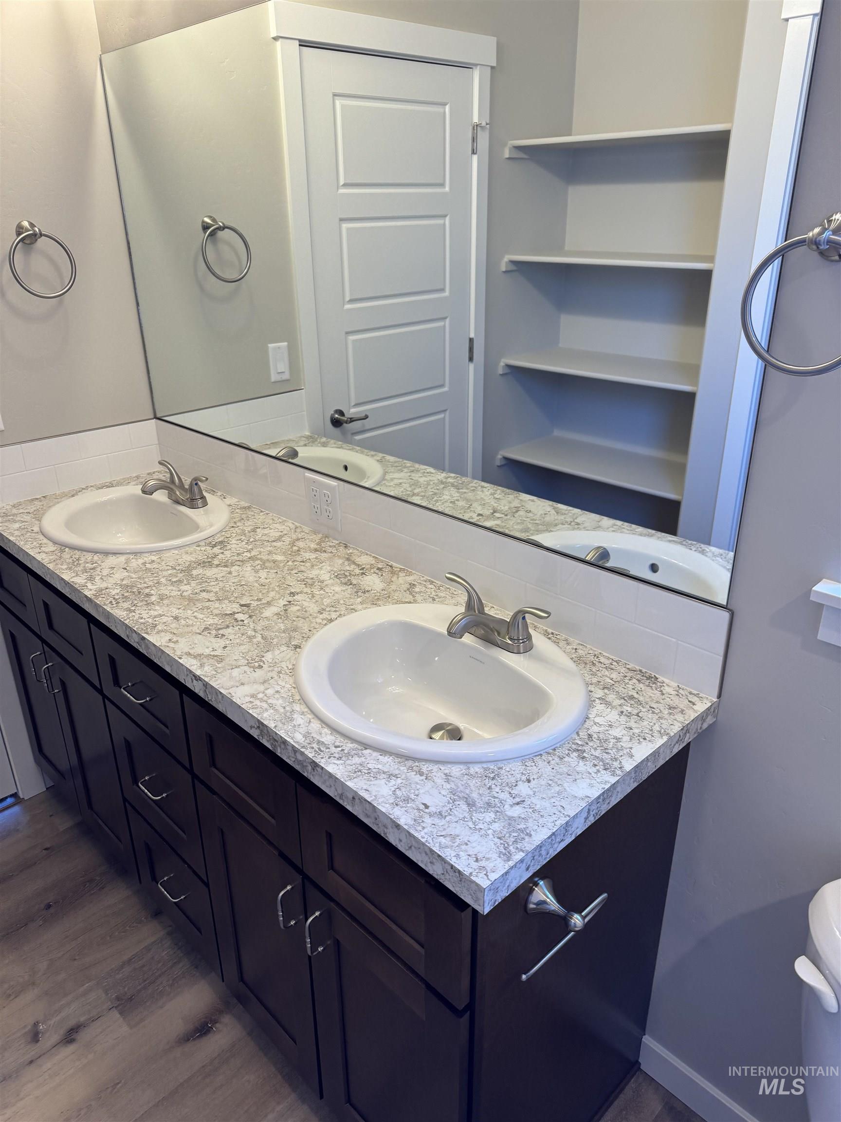 Full bath featuring double vanity and dark wood-style flooring