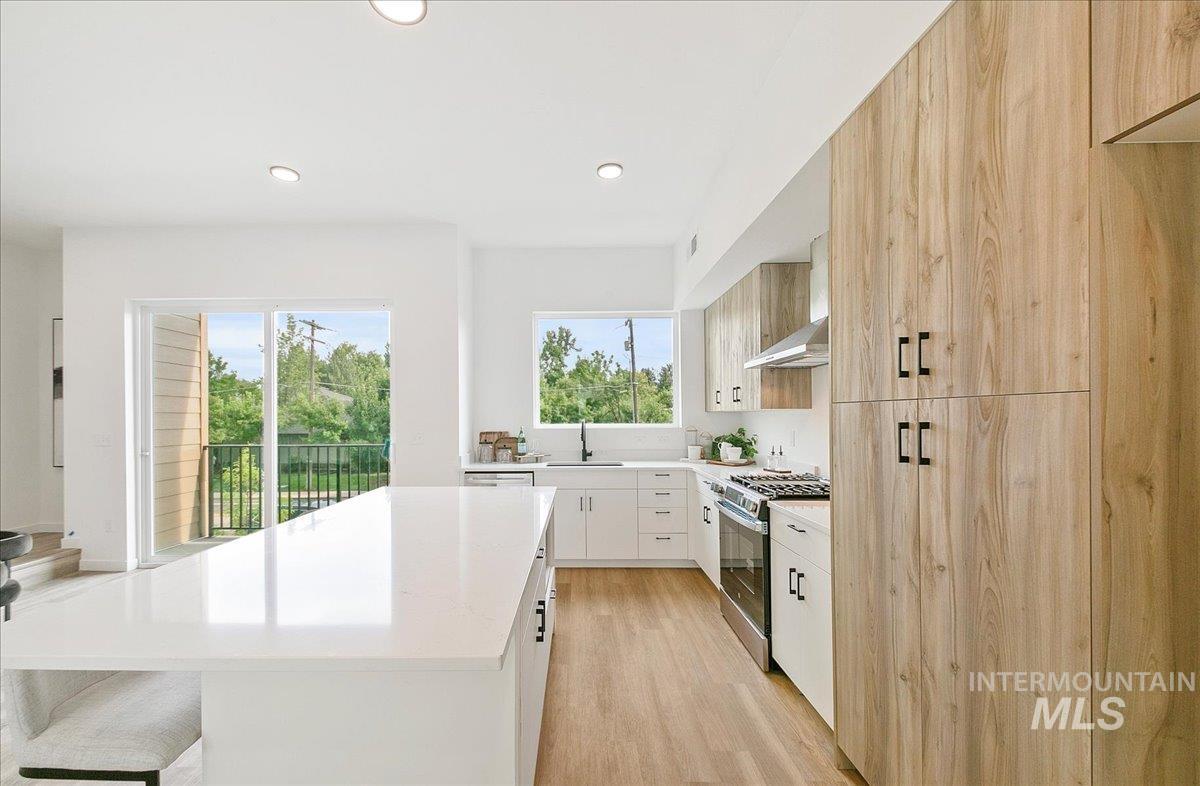 Kitchen with modern cabinets, light wood finished floors, gas stove, recessed lighting, and wall chimney range hood
